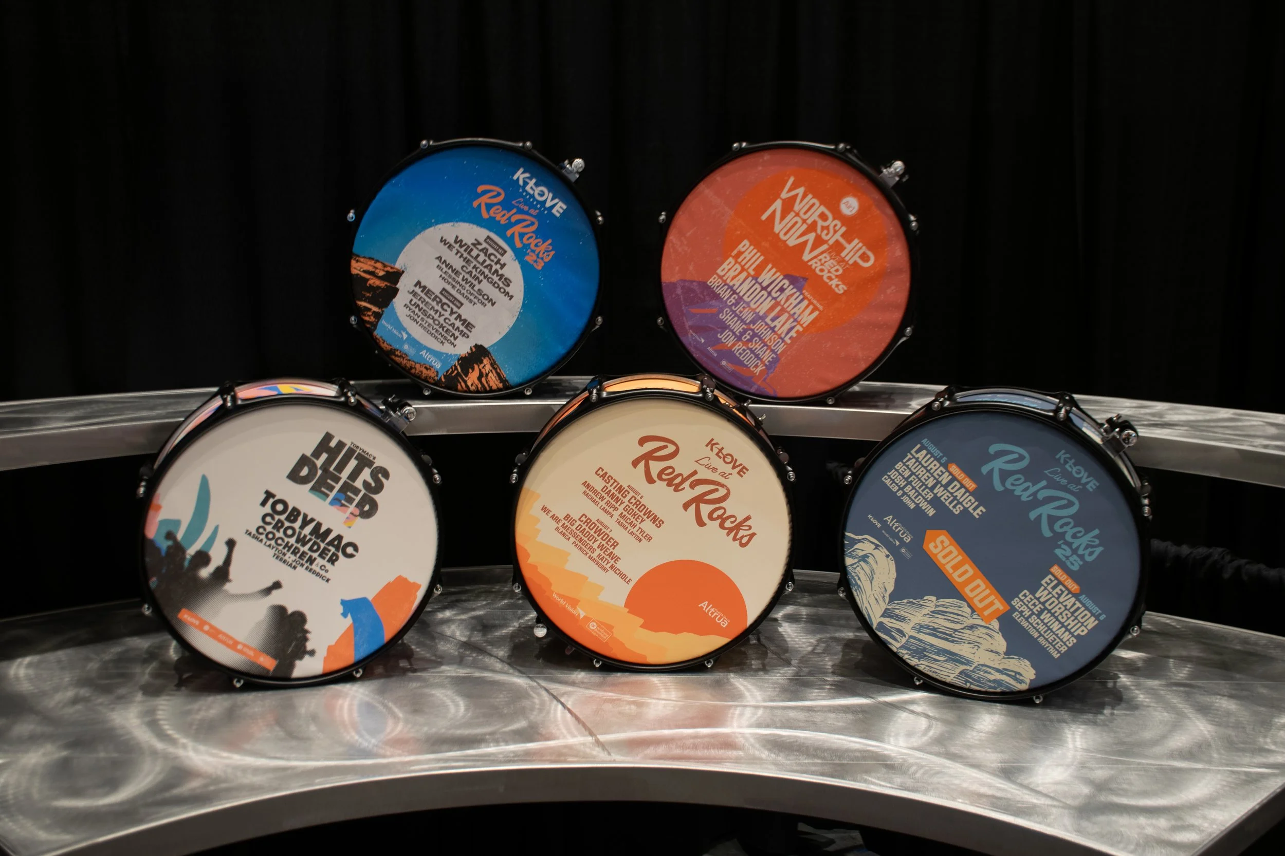Display of multiple drum awards with various colorful designs and text, arranged on a metal surface with a black background.