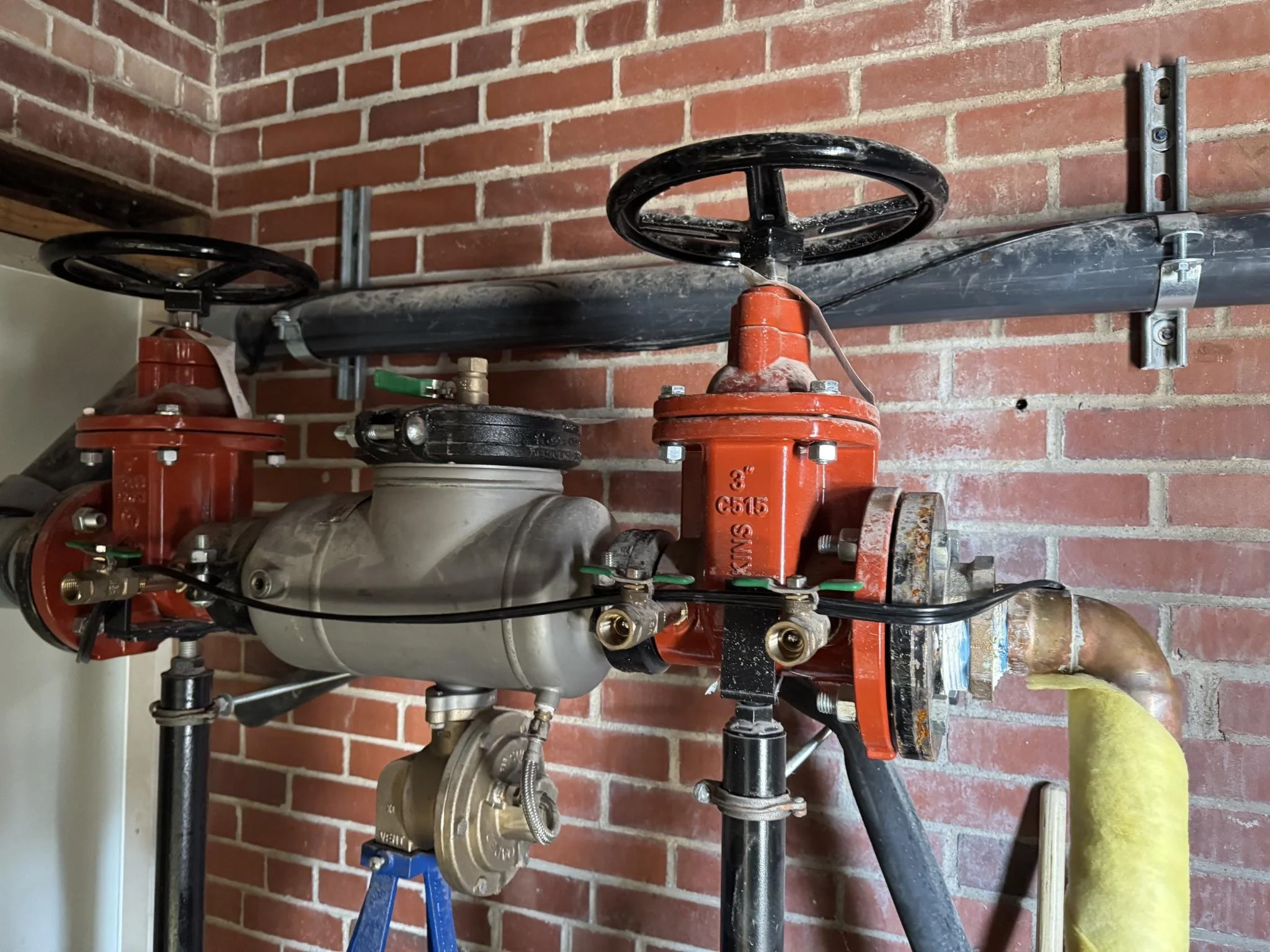 Fire sprinkler system with red valves and black piping installed on a red brick wall.