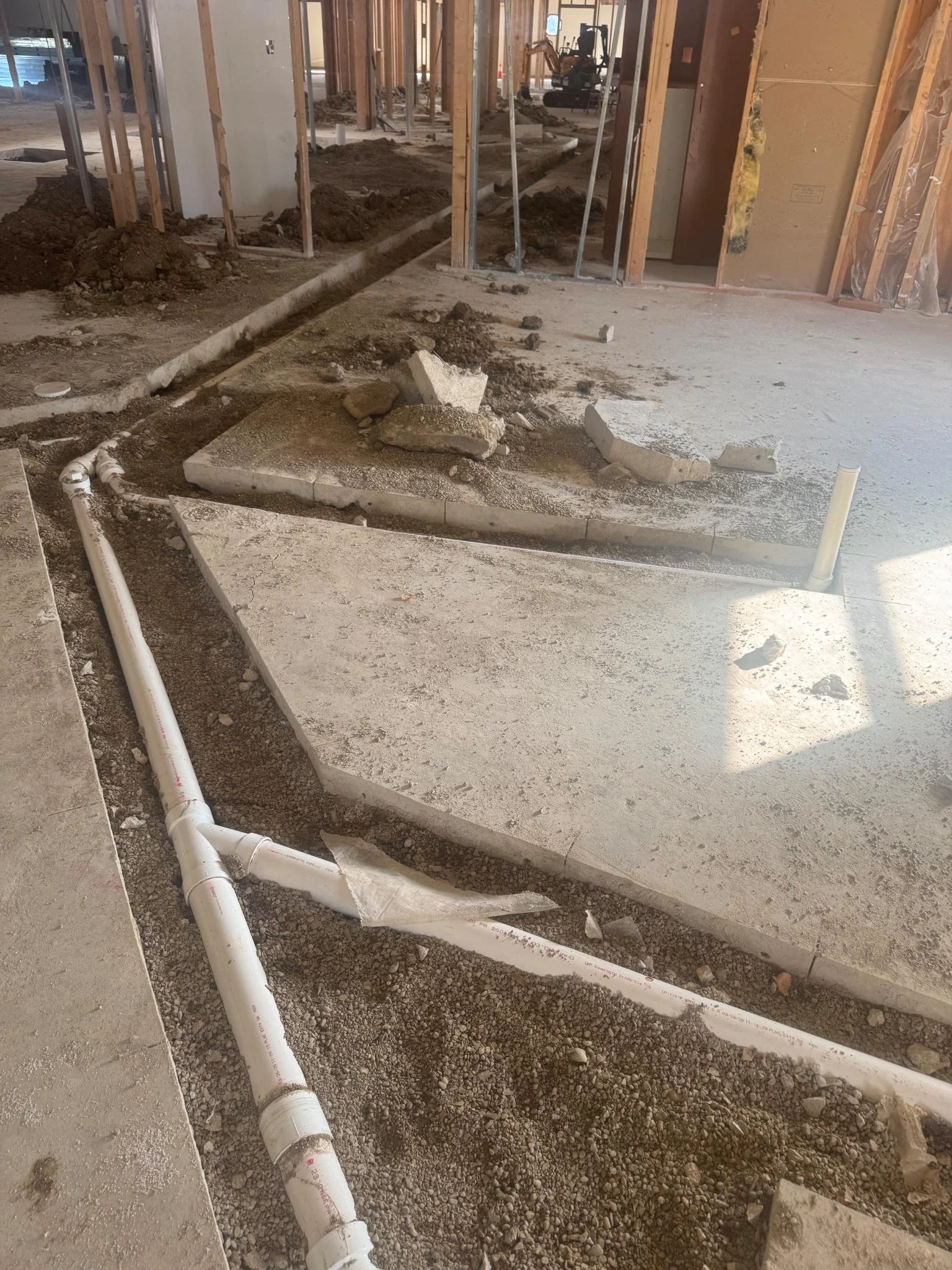 Construction site with exposed pipes and unfinished flooring, debris scattered around, in an indoor building under renovation.