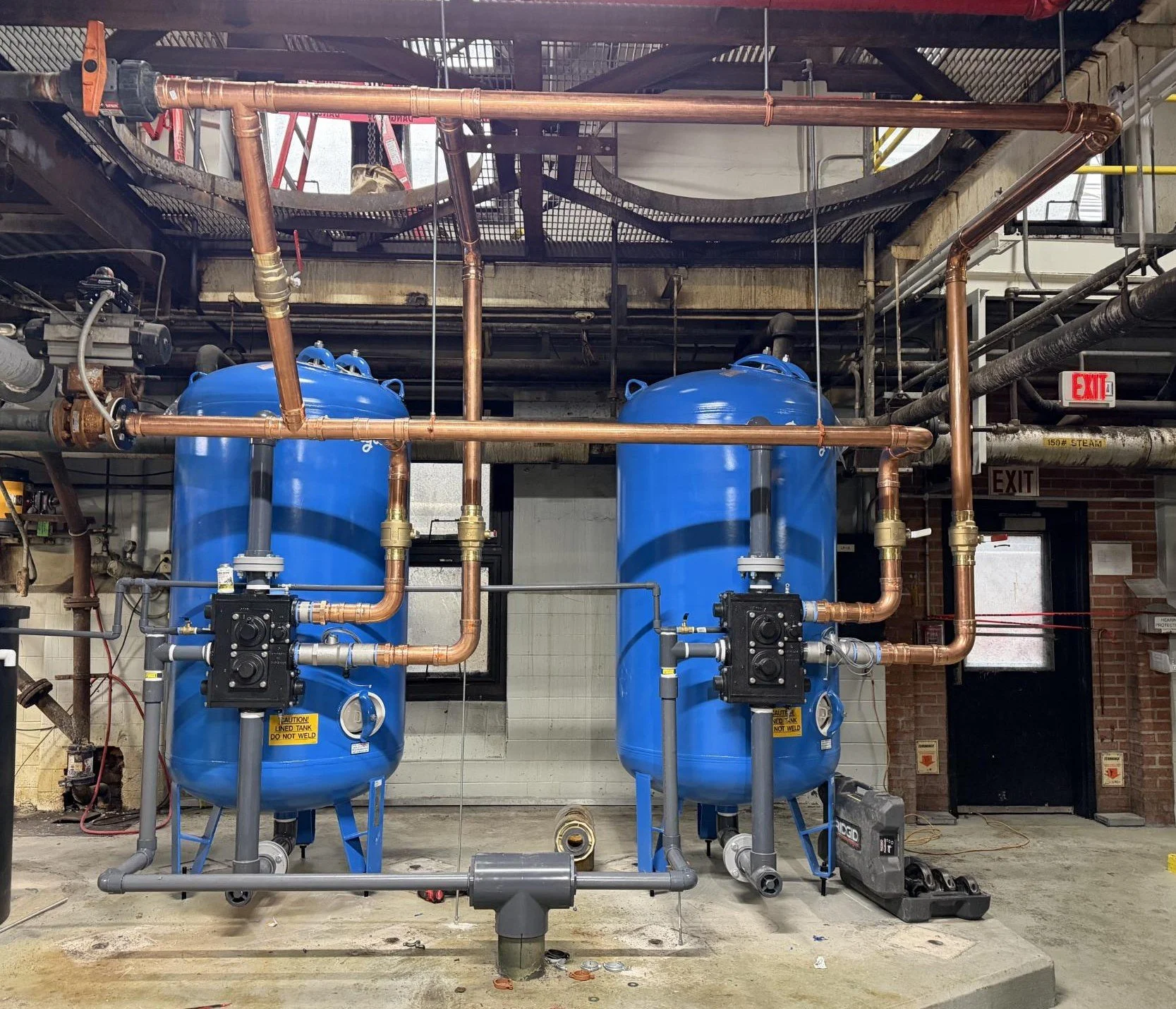 Two large blue tanks connected by copper pipes in an industrial setting with control valves and electrical equipment.