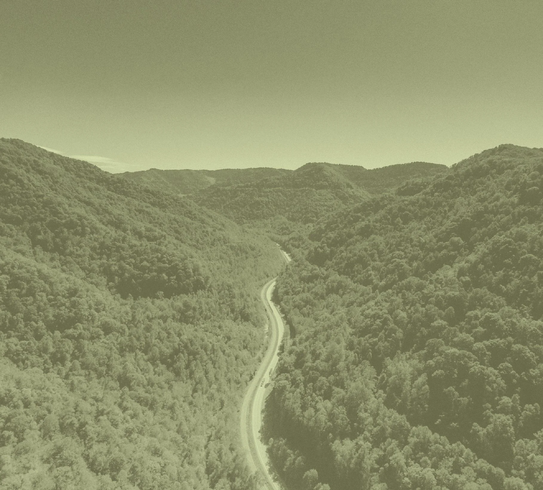 An aerial view of a winding road through a densely forested valley surrounded by mountains.