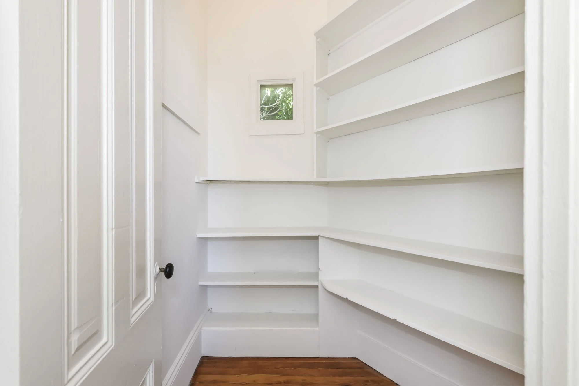 Small walk-in closet with white shelves and a small window.