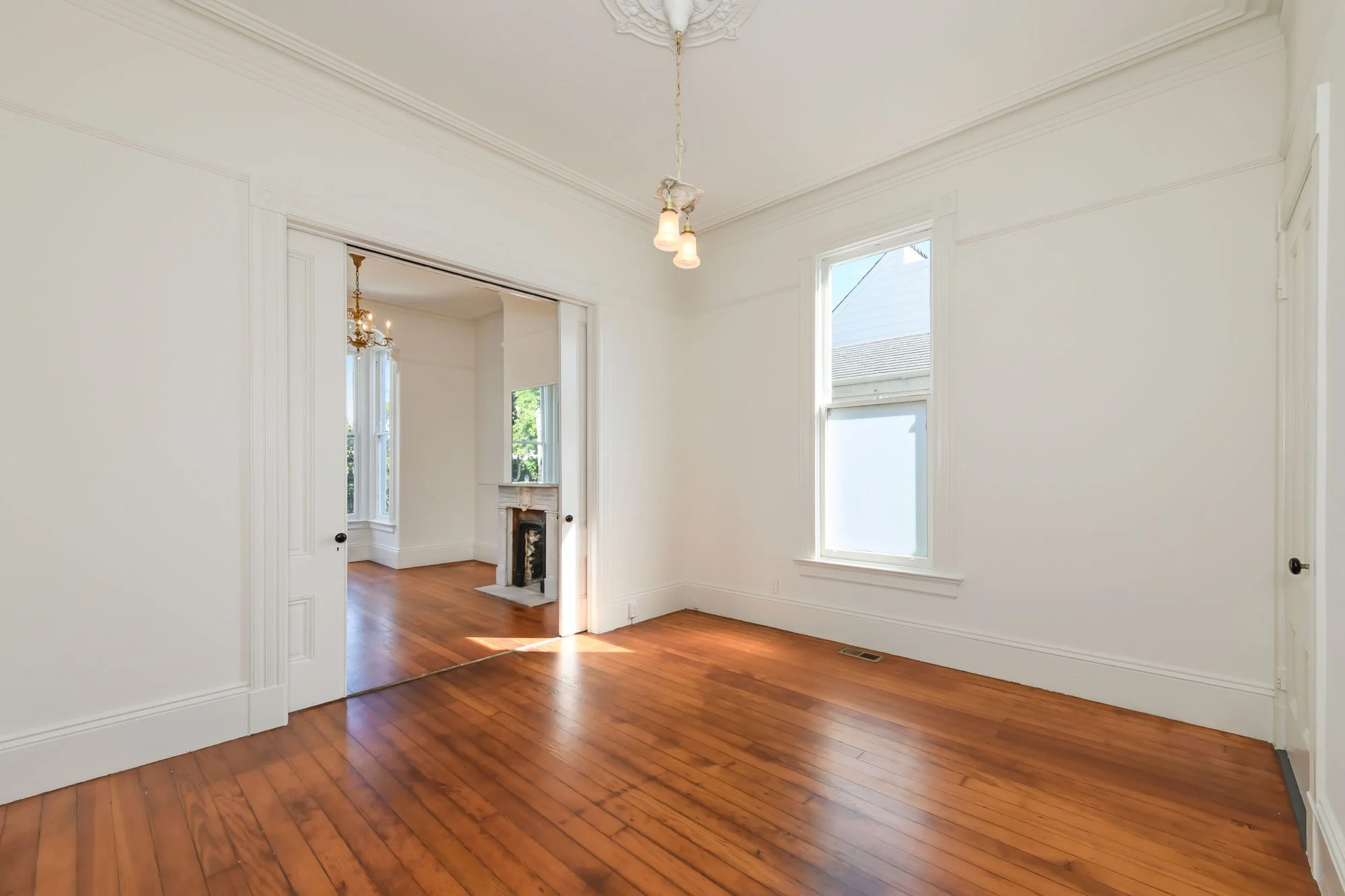 Empty room with white walls, hardwood floor, and large windows in a house.