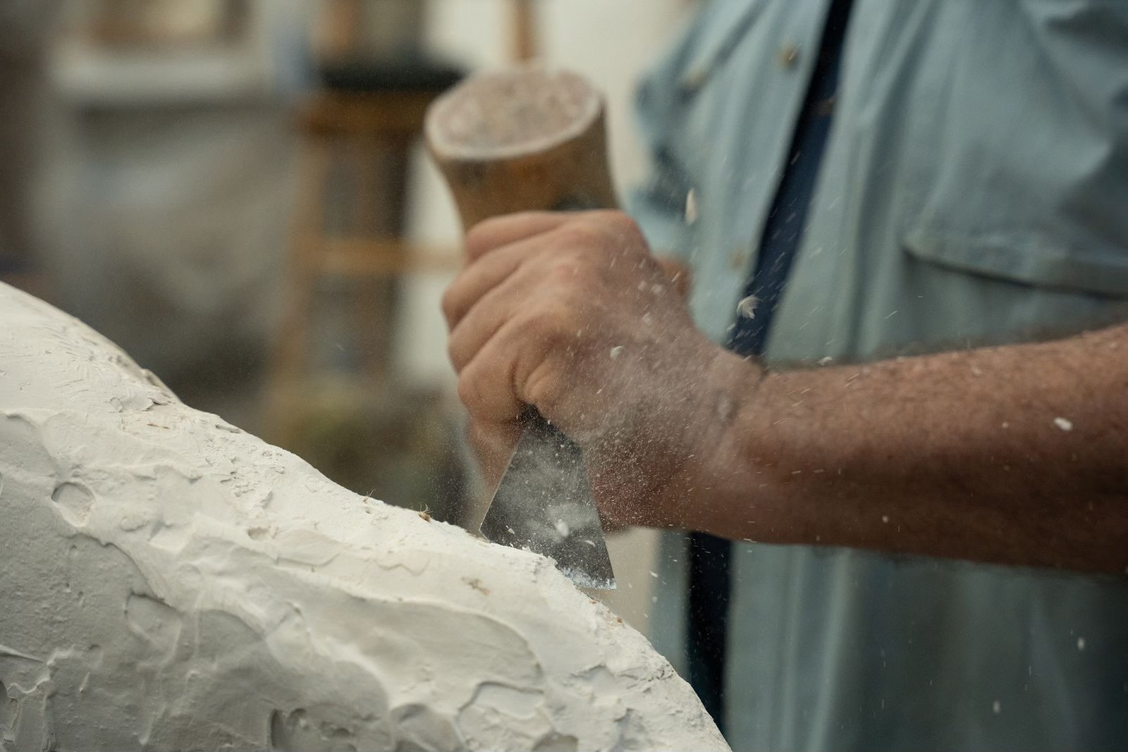 A person carving a piece of stone or marble with a handheld tool, creating dust and chips
