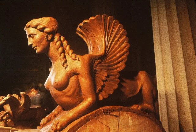 Clay sculpture of a mythological creature with a woman's head, braids, and a large feathered tail, details of the helmet on Athena Parthenos in Parthenon Museum Nashville. 