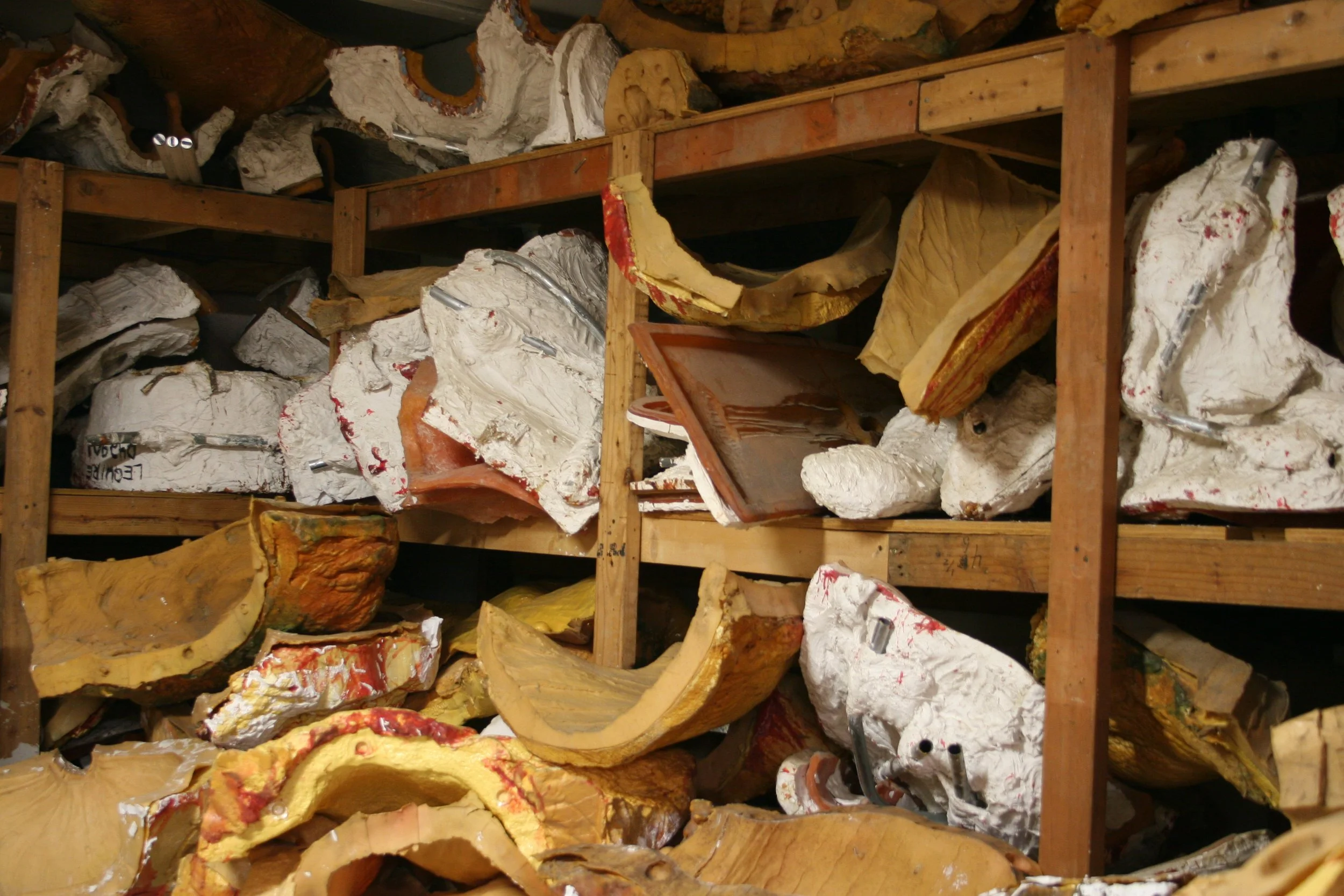 Shelf holding large, irregularly shaped molds of sculptures in a workshop or storage space.