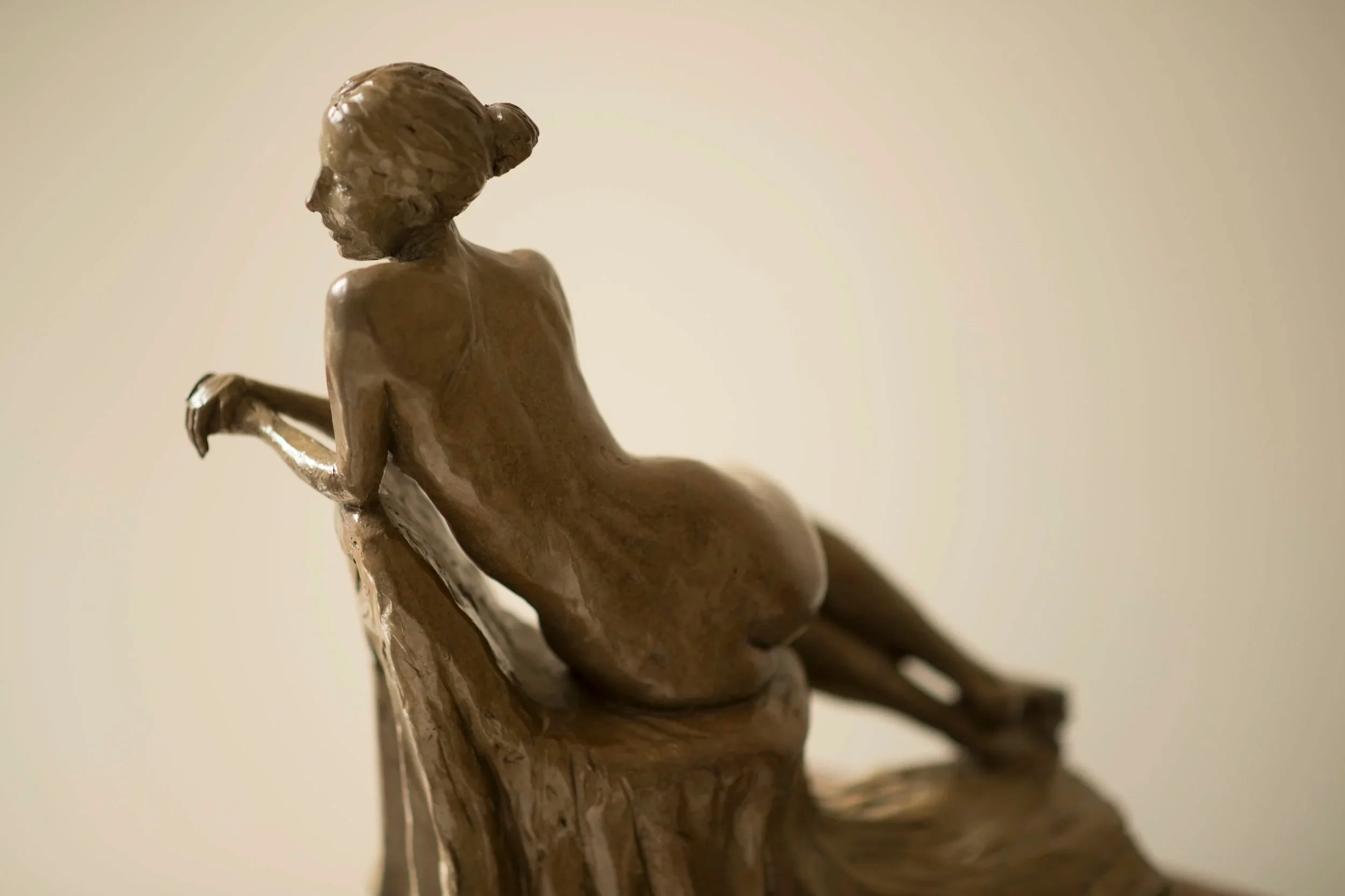 Close-up of a wooden sculpture of a reclining woman with her hair tied back, viewed from the side against a plain background.