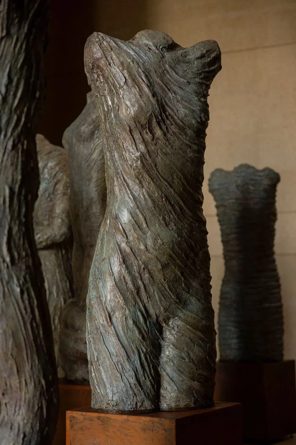 Close-up of a textured, abstract sculpture with swirling grain patterns, displayed indoors on a metal pedestal.