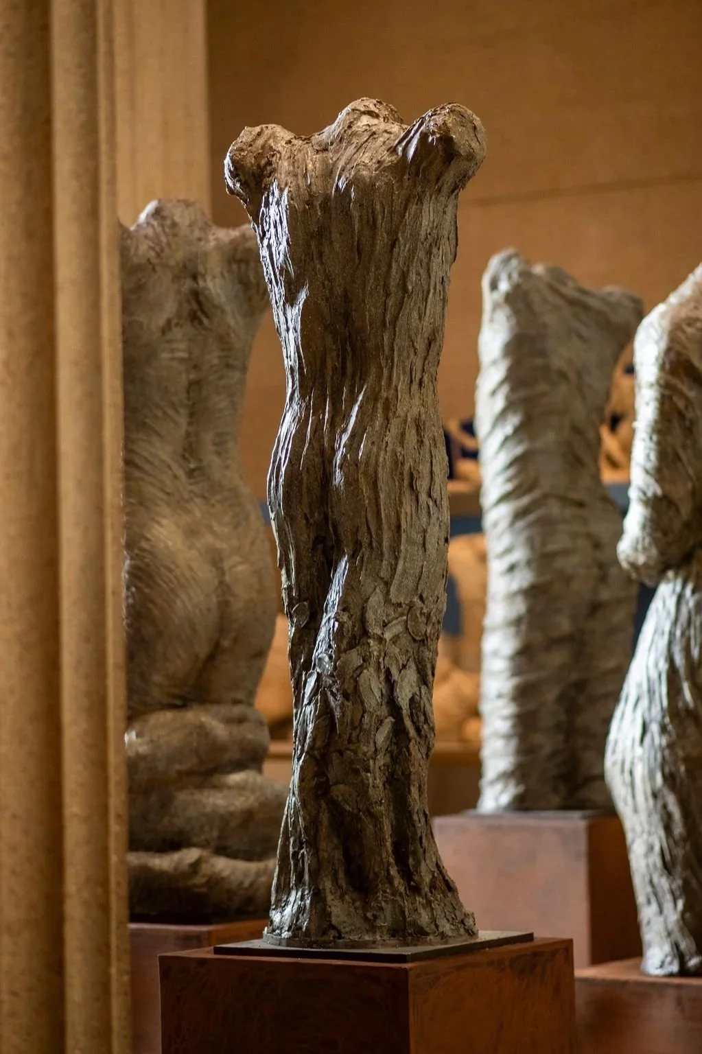 Plaster sculpture resembling a human torso with detailed texture, displayed on a metal pedestal in an art gallery.