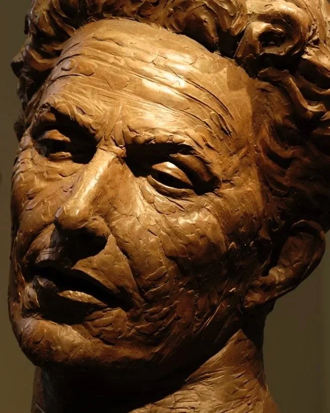 Close-up of a bronze bust sculpture of a Woody Guthries head, showcasing detailed facial features and textured hair, in a museum setting.  Cultural Heroes