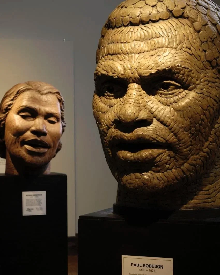 Two realistic sculptures of human heads on display in a museum.  Cultural Heroes