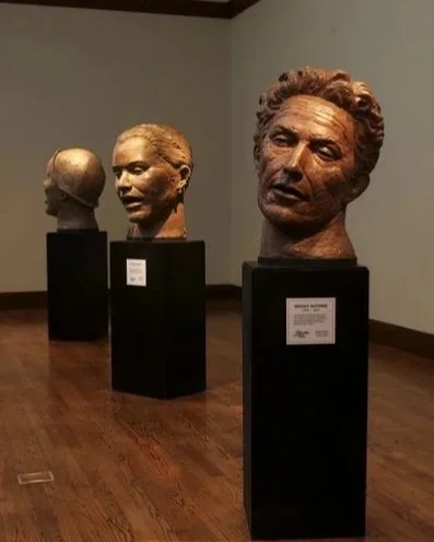 Three bust sculptures displayed on black pedestals in a gallery with hardwood floors and light-colored walls.  Cultural Heroes