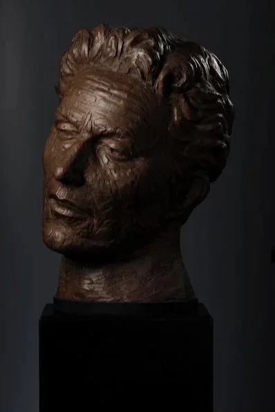 Bronze sculpture of a Woody Guthry’s head with curly hair, set against a dark background.  Cultural Heroes