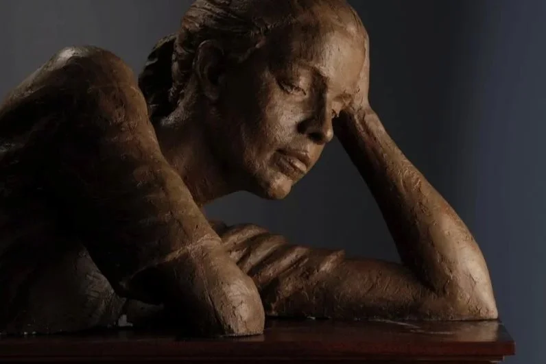 Bronze sculpture of a woman resting her head on her hand with a contemplative expression.