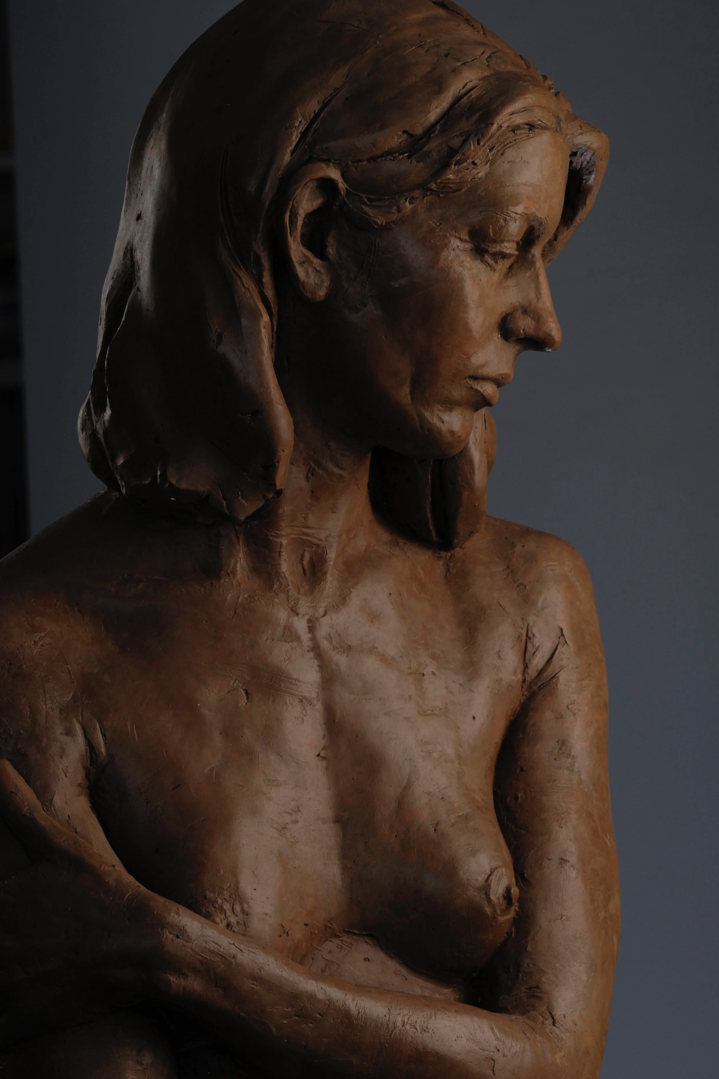 Close-up of a bronze sculpture of a woman with closed eyes, long hair, and a somber expression.