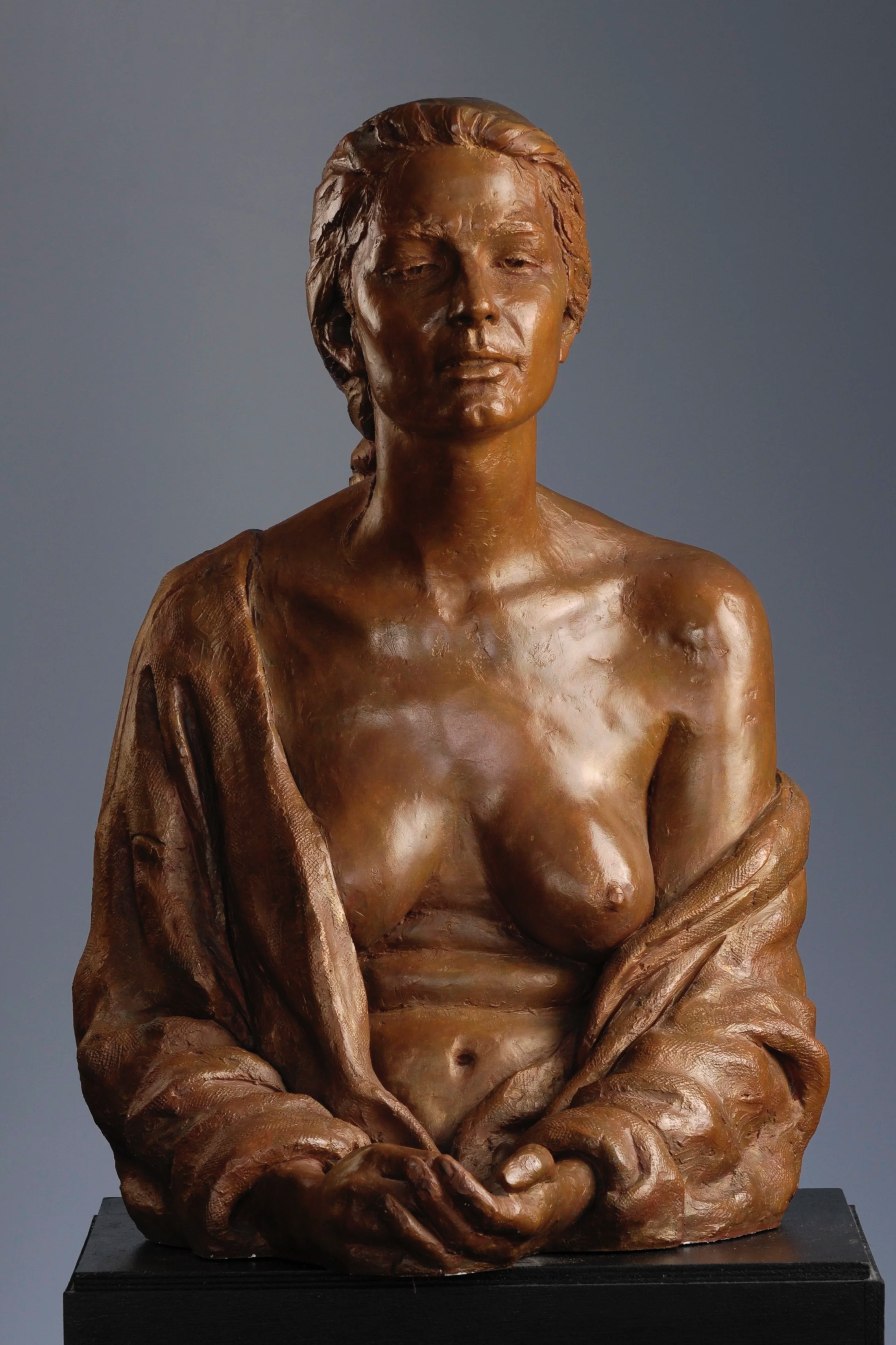 Bronze bust sculpture of a woman with closed eyes, draped in a shawl, sitting on a black pedestal against a neutral background.