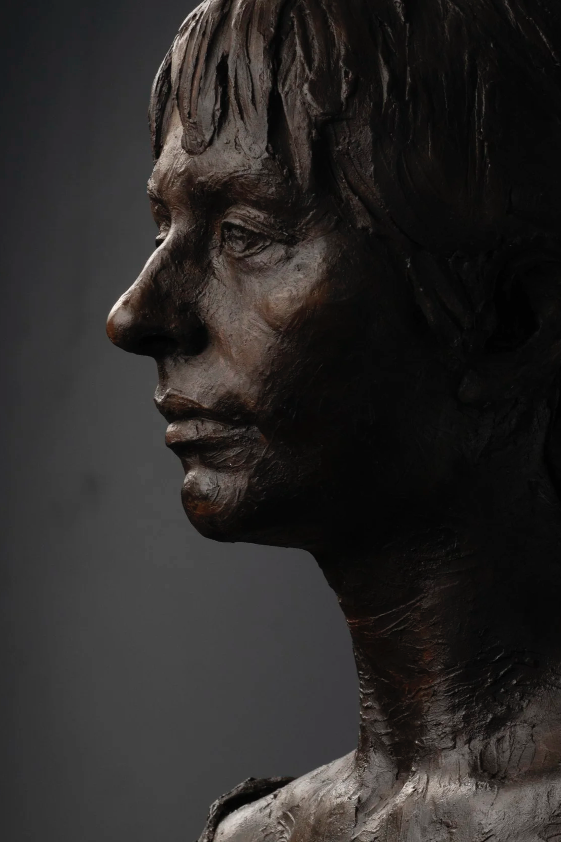 Bronze bust sculpture of a woman's profile with short hair against a dark background.