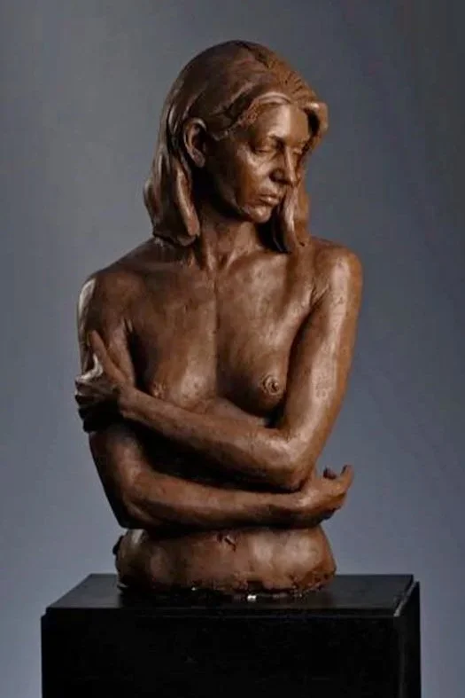 Bronze sculpture of a woman with her arms crossed, looking downward with a contemplative expression.