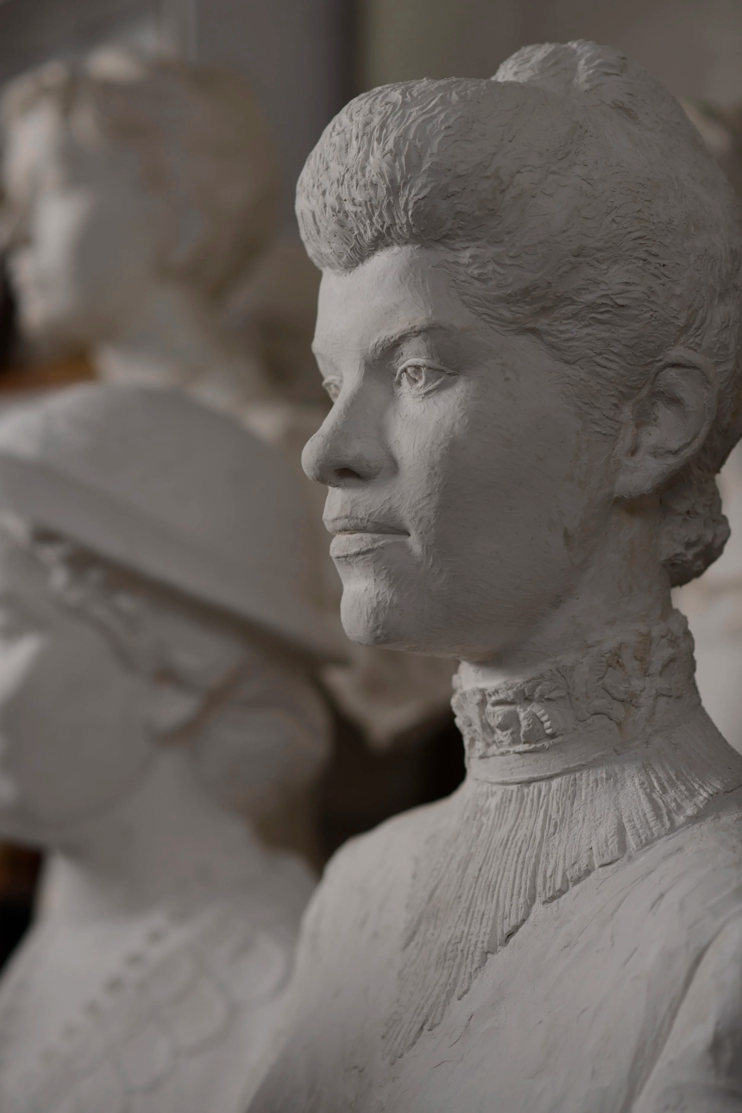 Close-up of white plaster bust sculptures of historical figures, with detailed facial features and textured hair, displayed in an art studio or gallery. Ida B Wells. Woman Suffrage