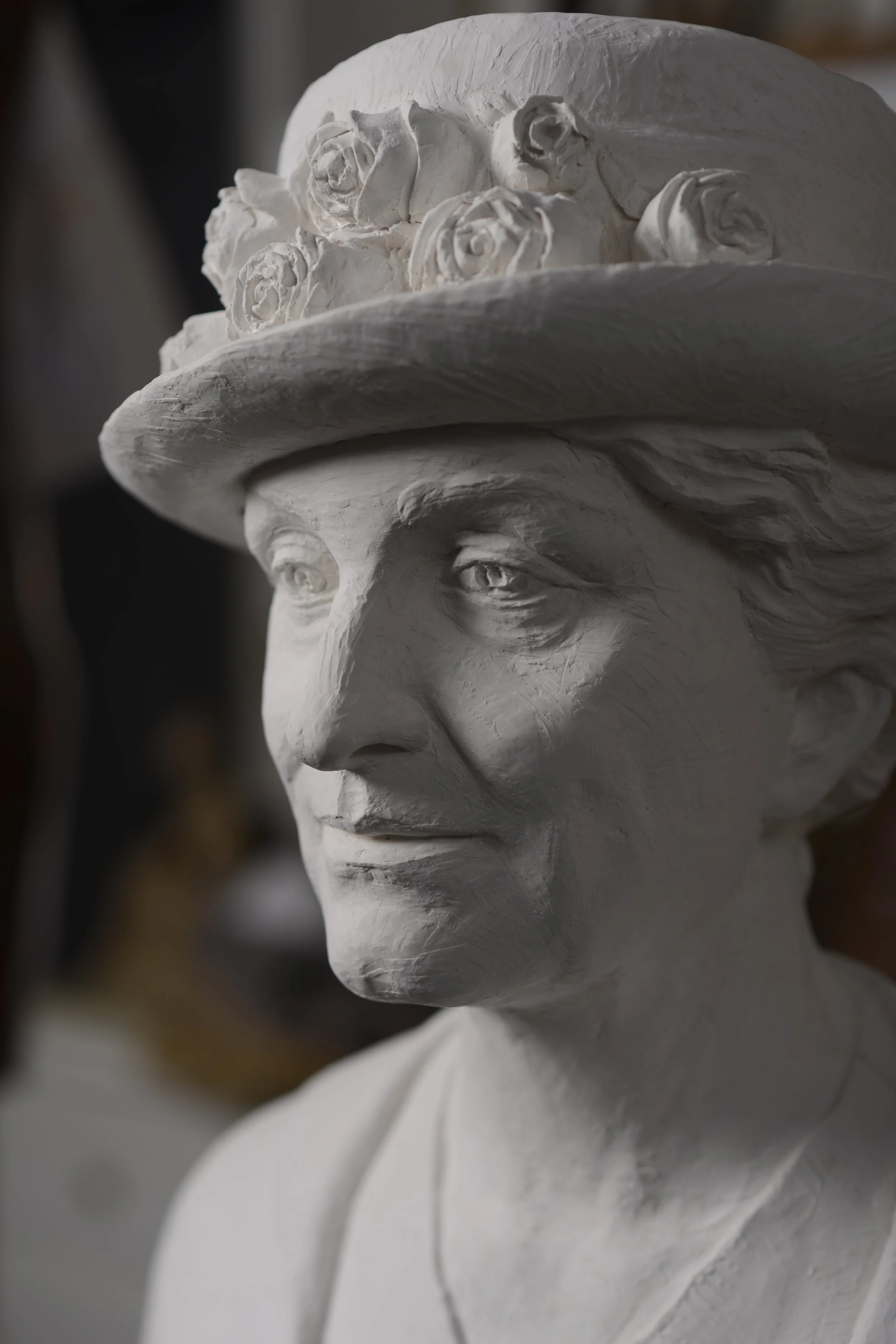 Close-up of a white plaster bust sculpture of a person's face with a wide-brimmed hat, detailed facial features, and textured surface. Woman Suffrage