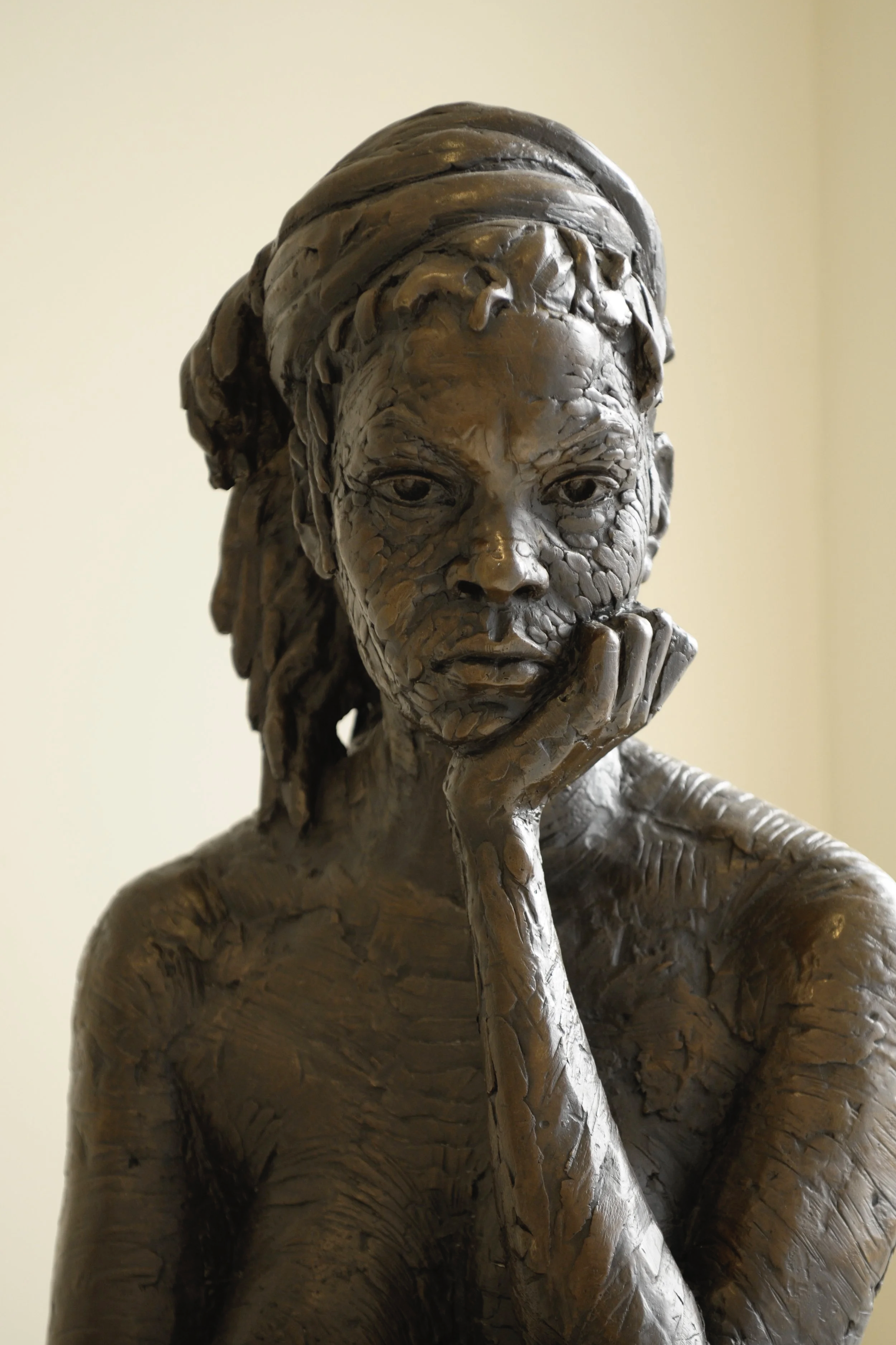 Close-up of a bronze sculpture of a woman with her hand on her chin, with detailed hair and facial features.