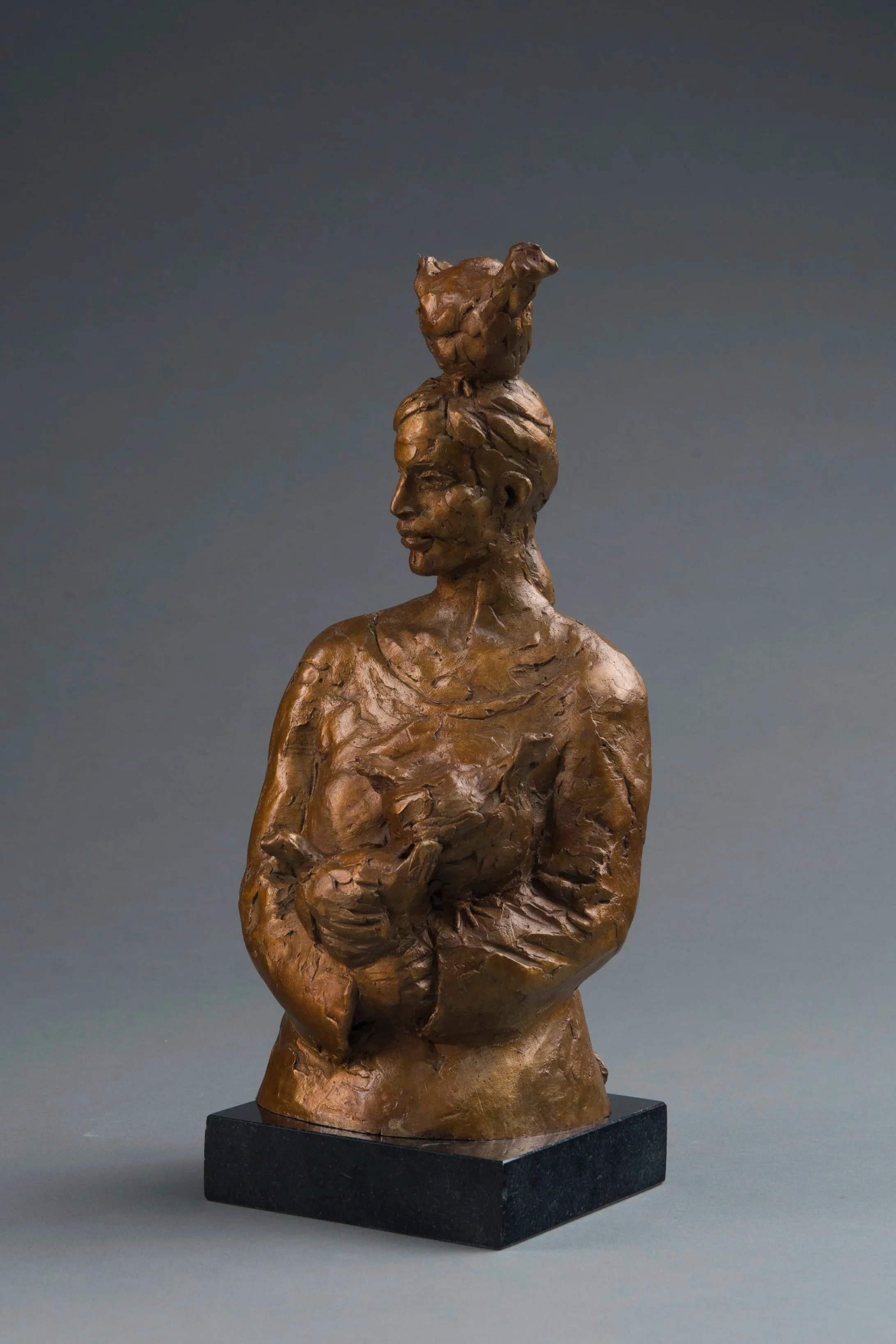 A sculpture of a woman with a chicken on her head, set against a plain dark background.