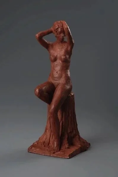 A sculpture of a seated woman with one arm raised behind her head, sitting.