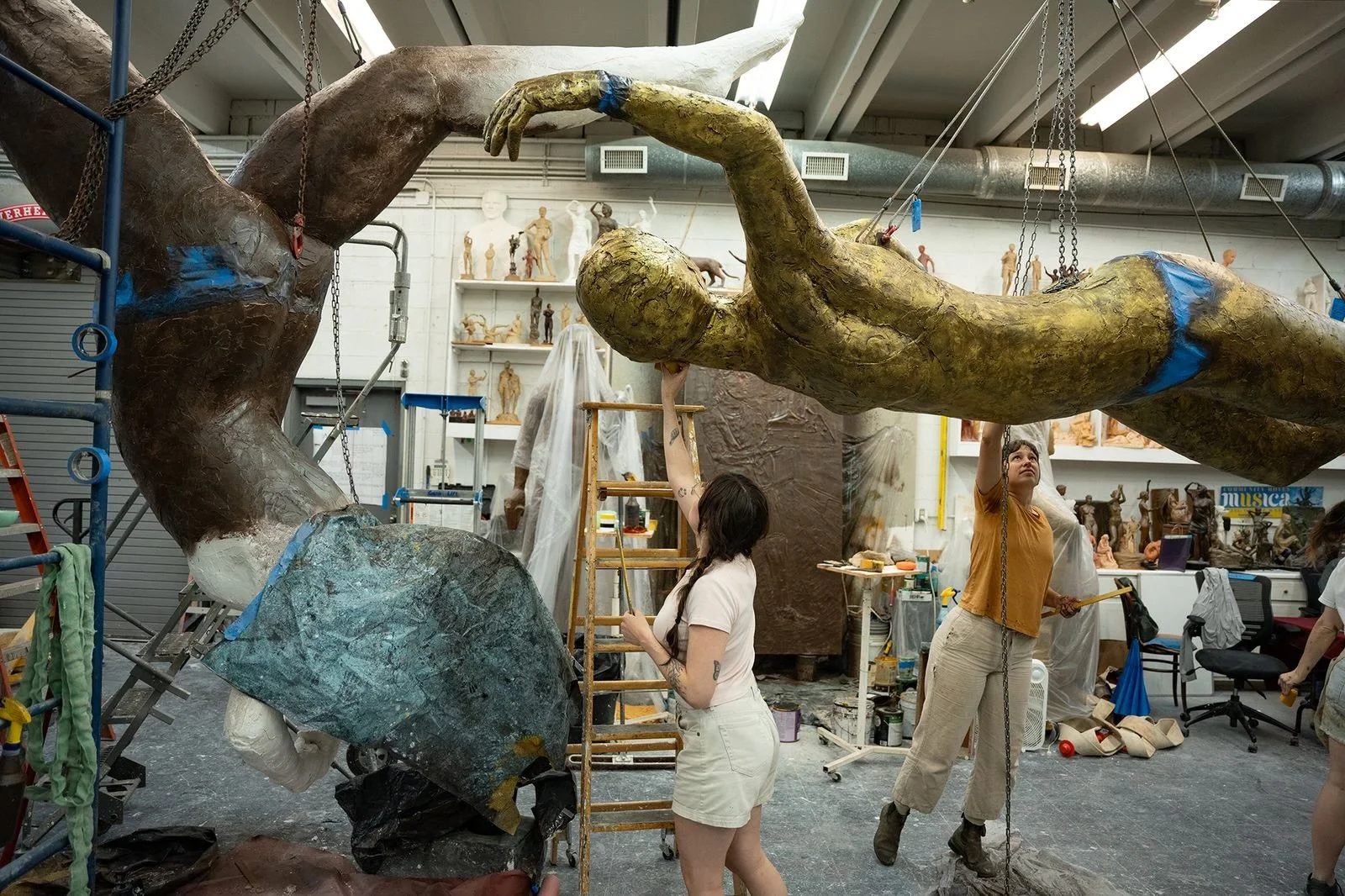Artists working on large sculptures in a studio with various art supplies and sculptures in the background.