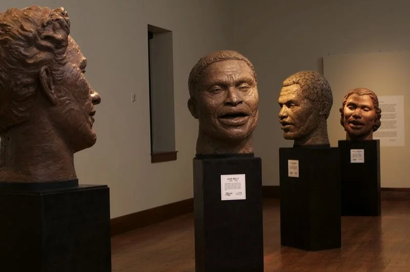 Four bronze bust sculptures of African American individuals displayed on black pedestals in an art gallery.  Cultural Heroes