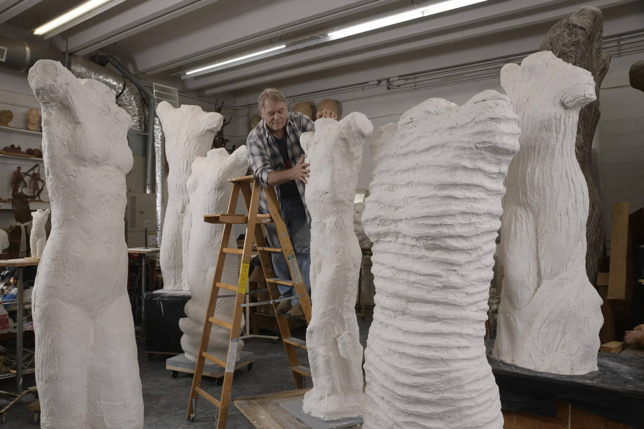 An artist working on large, white, textured sculptures in an art studio. The sculptures resemble abstract trees or figures.