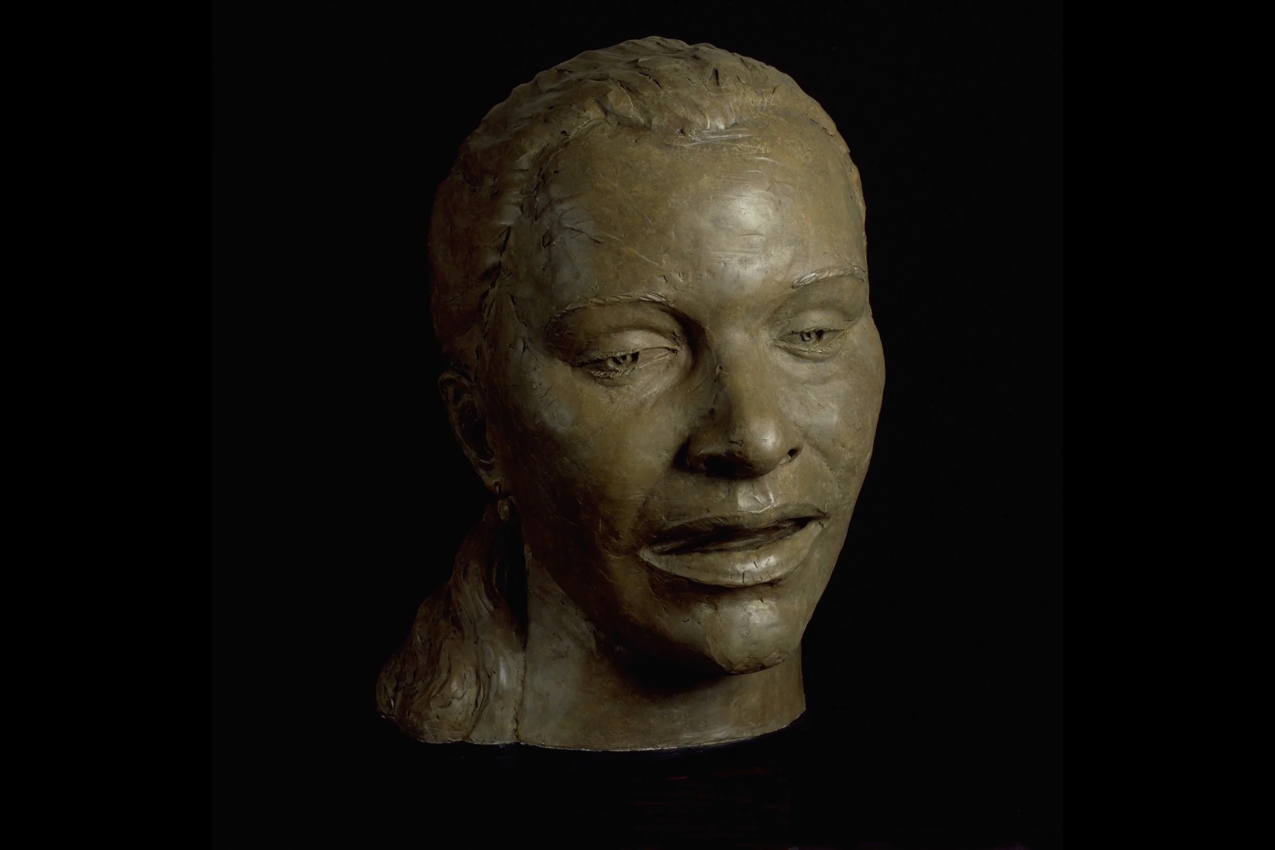 Close-up of a bronze bust sculpture of an Asian woman with braided hair, against a black background.