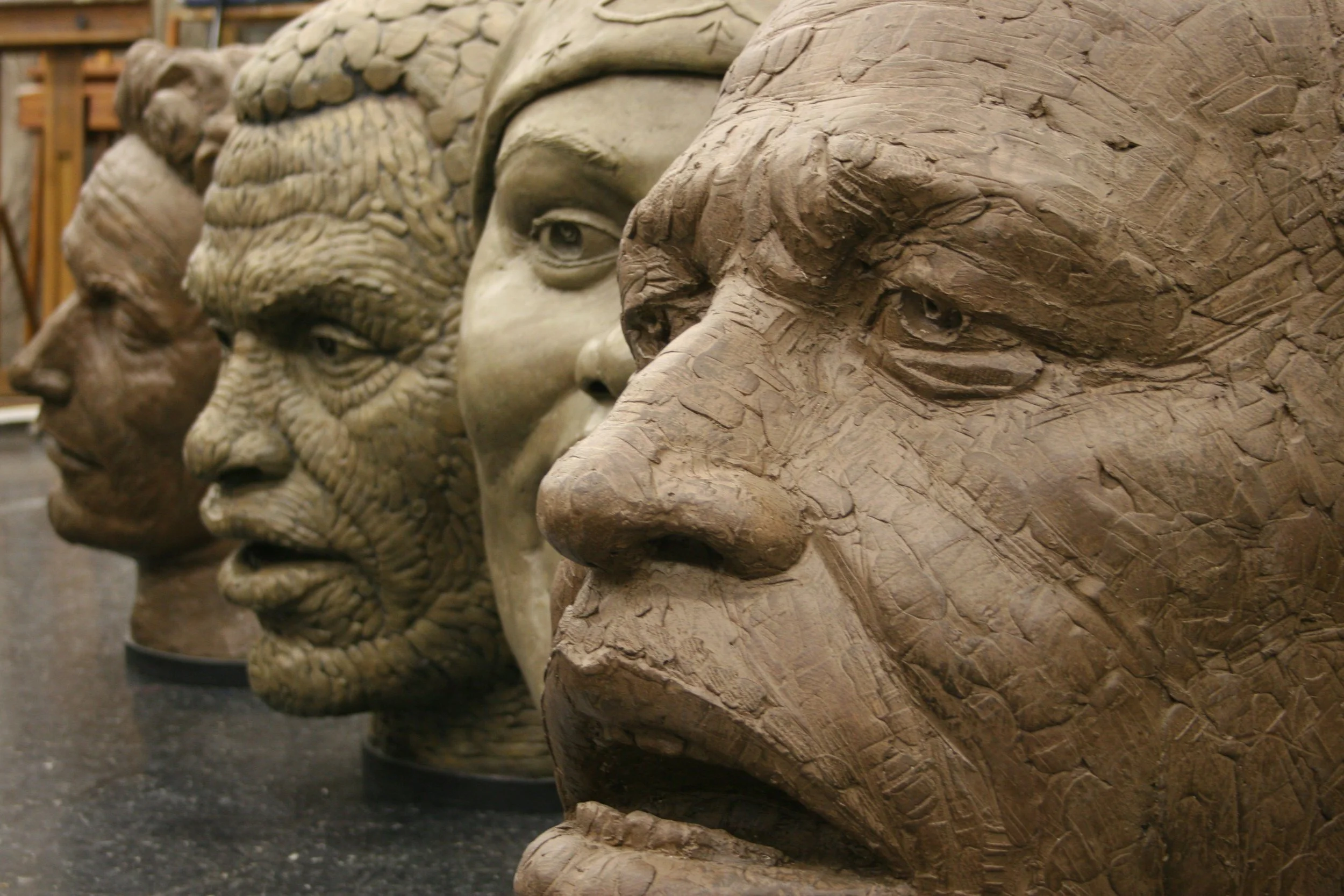 Close-up of a row of detailed plaster sculptures of faces from the cultural heroes series with a background of shelves and woodwork.  Cultural Heroes