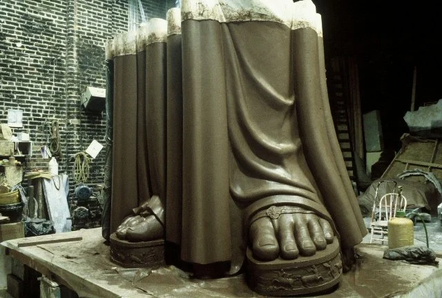 Close-up of a sculpture in progress featuring large, detailed feet and legs in a workshop setting. Athena Parthenos in Parthenon Museum Nashville. 