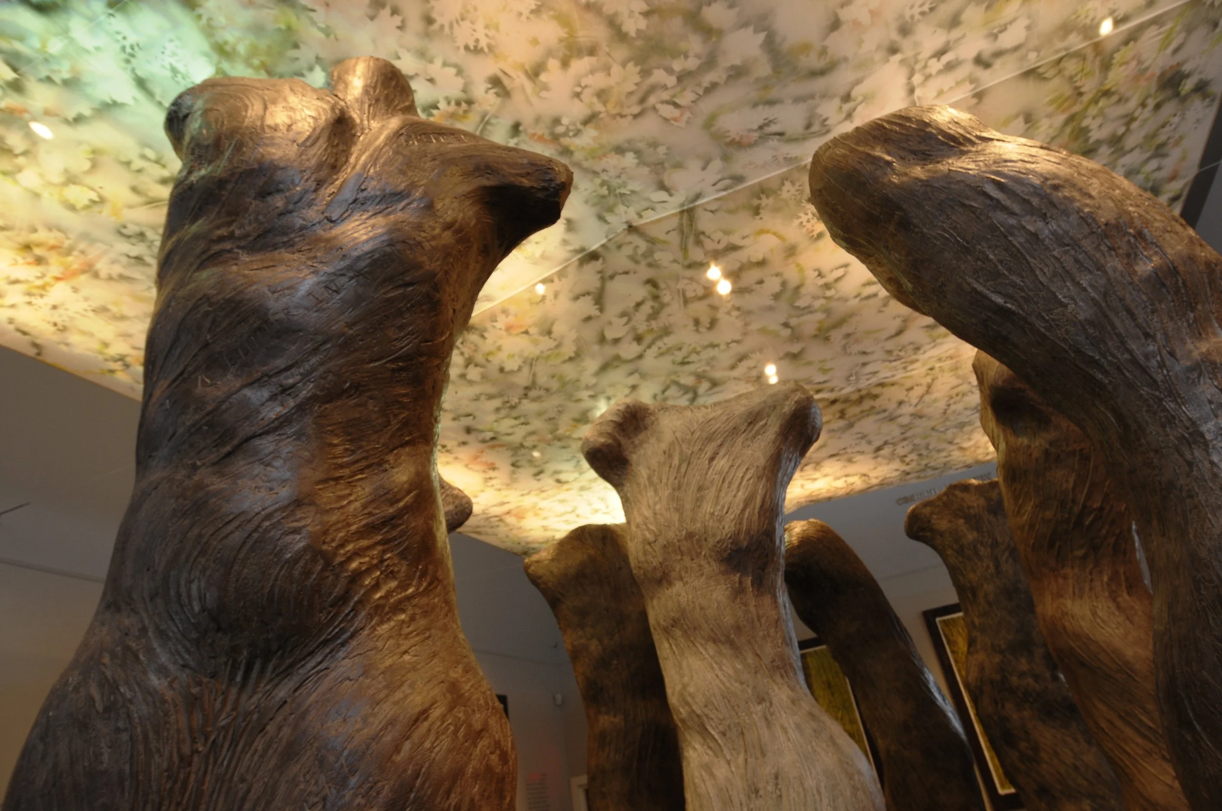 Close-up view of large wooden sculptures resembling tree trunks with a floral-patterned ceiling and lighting in the background. Dream Forest Installation. 