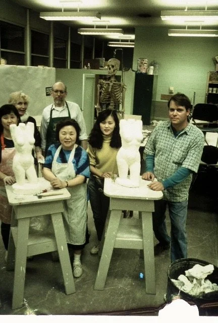 Group of six people in a pottery studio standing behind two ceramic cat sculptures on pedestals.