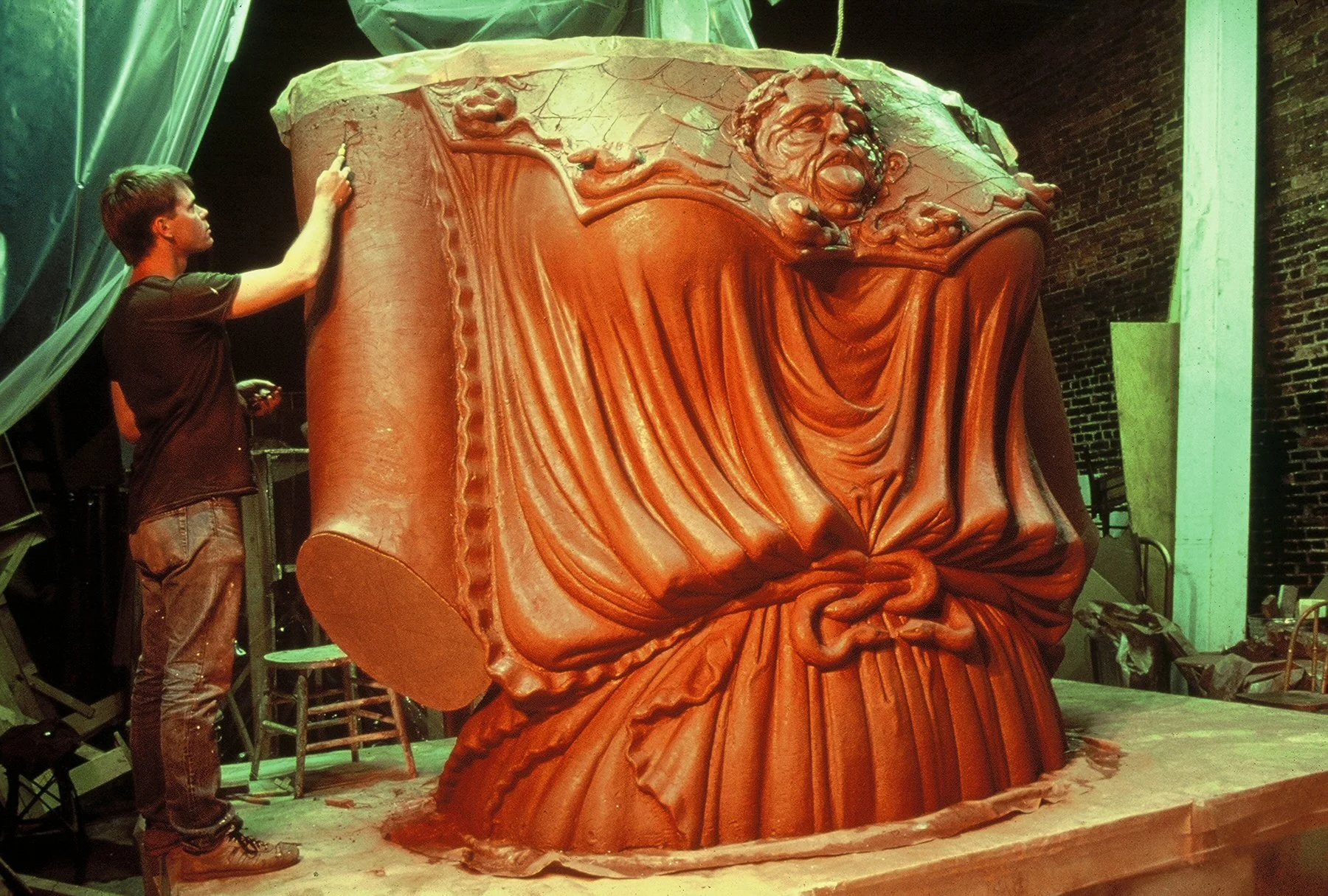 A young man working on carving a large clay sculpture of a Athena Parthenos in a workshop with brick walls. Athena Parthenos in Parthenon Museum Nashville. 