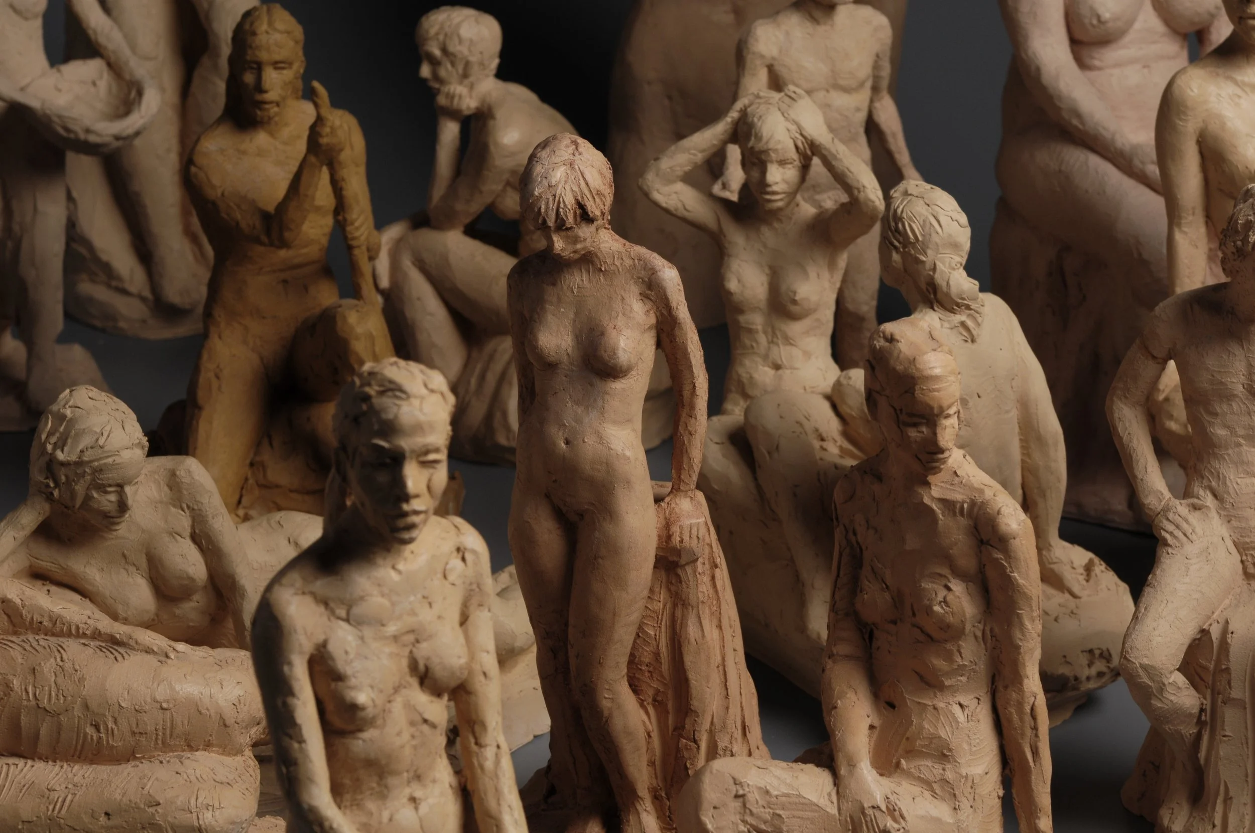 A collection of beige clay sculptures depicting various human figures, including seated, standing, and expressive poses, arranged closely together.