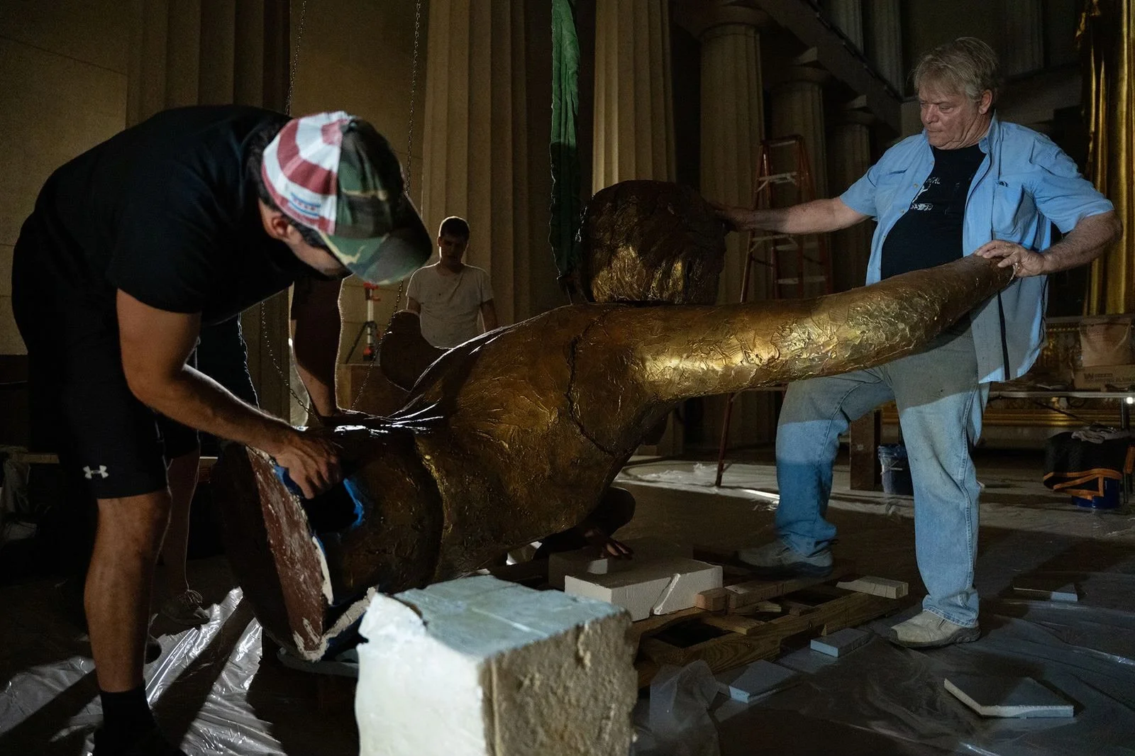 People working on a large sculpture of a whale in a dimly lit studio.