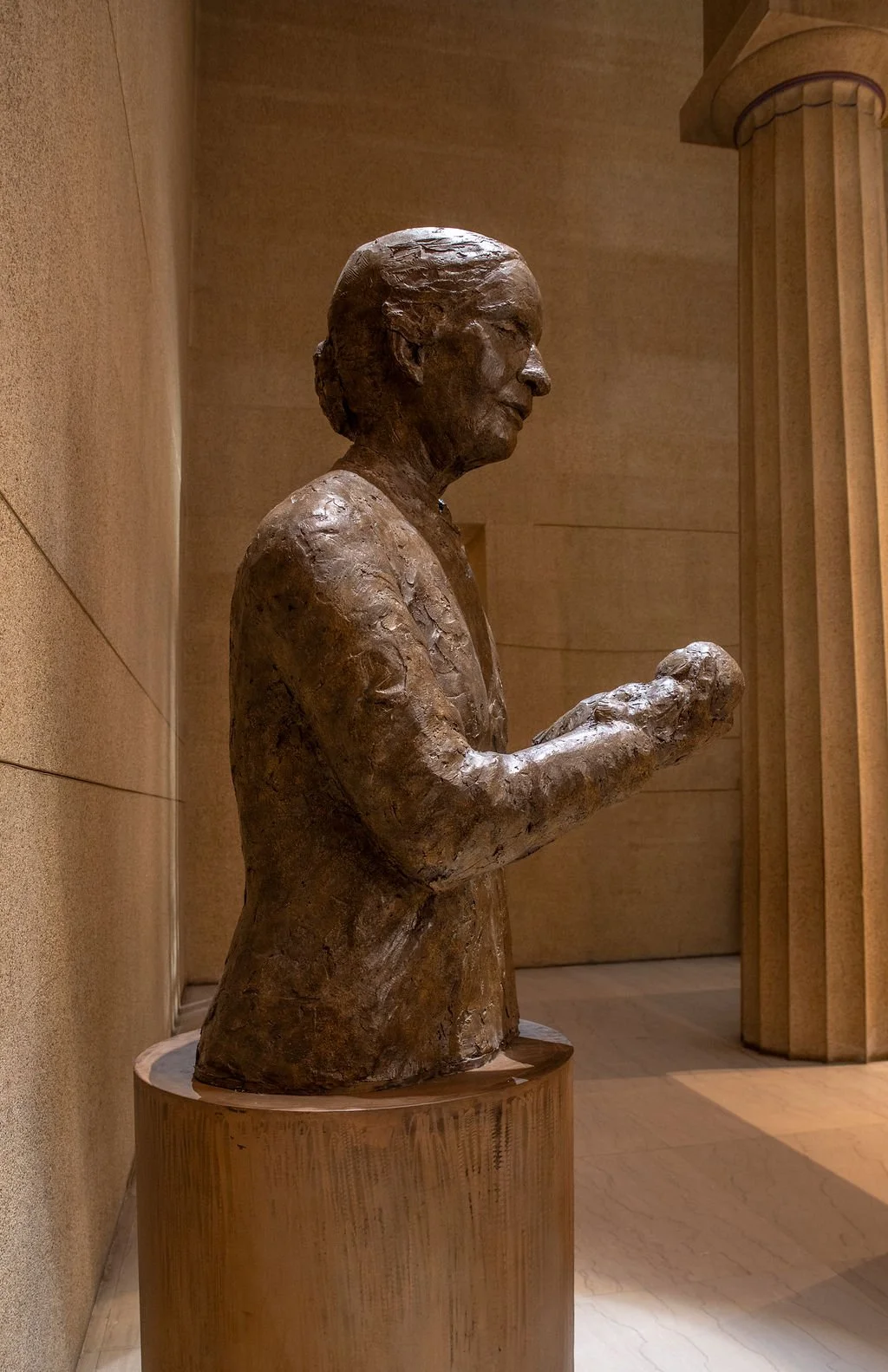 Bronze sculpture of a woman holding a baby. displayed on a metal pedestal in an indoor setting.