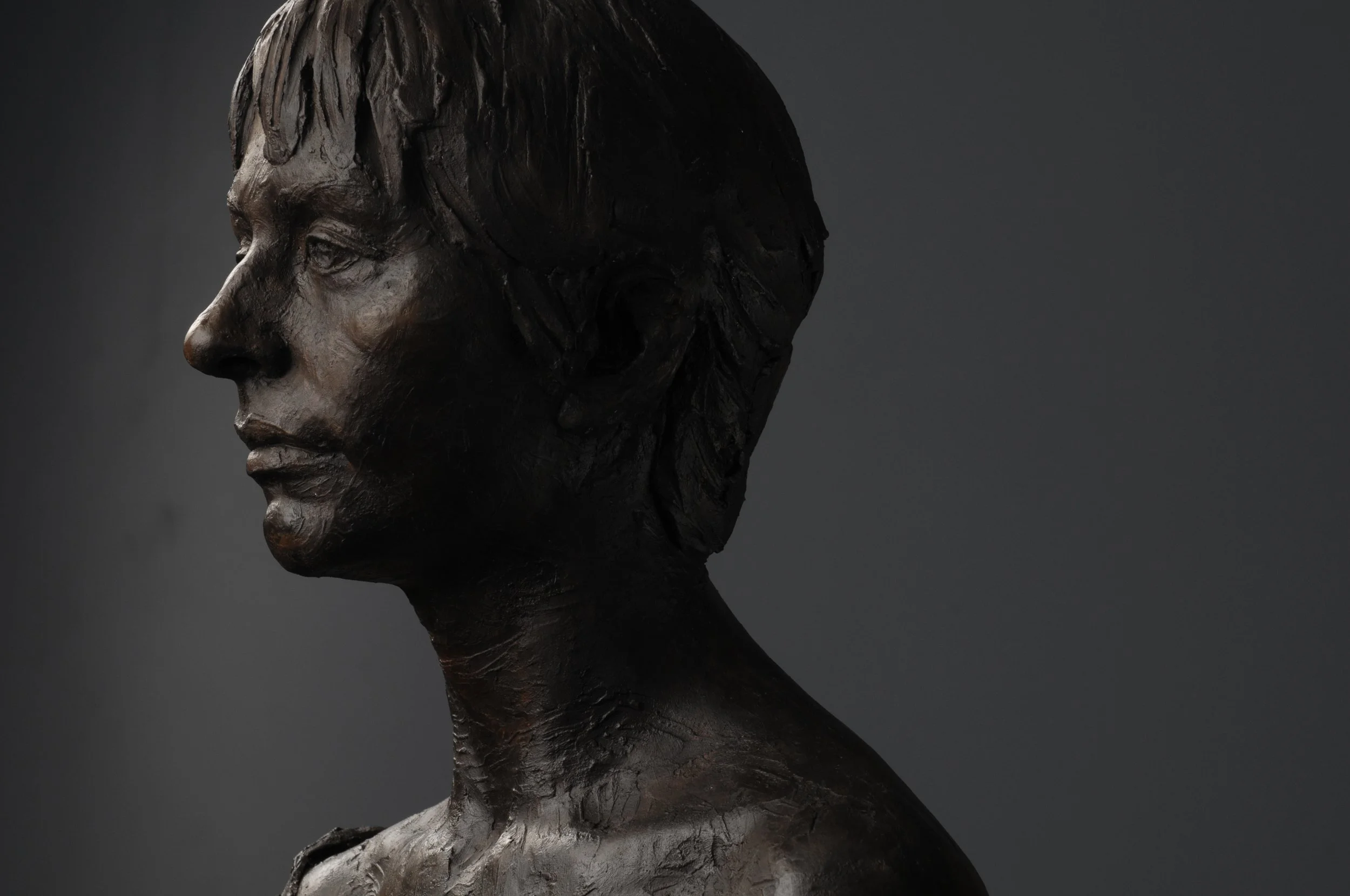 Close-up of a dark-colored sculpture of a woman's face in profile against a dark background.