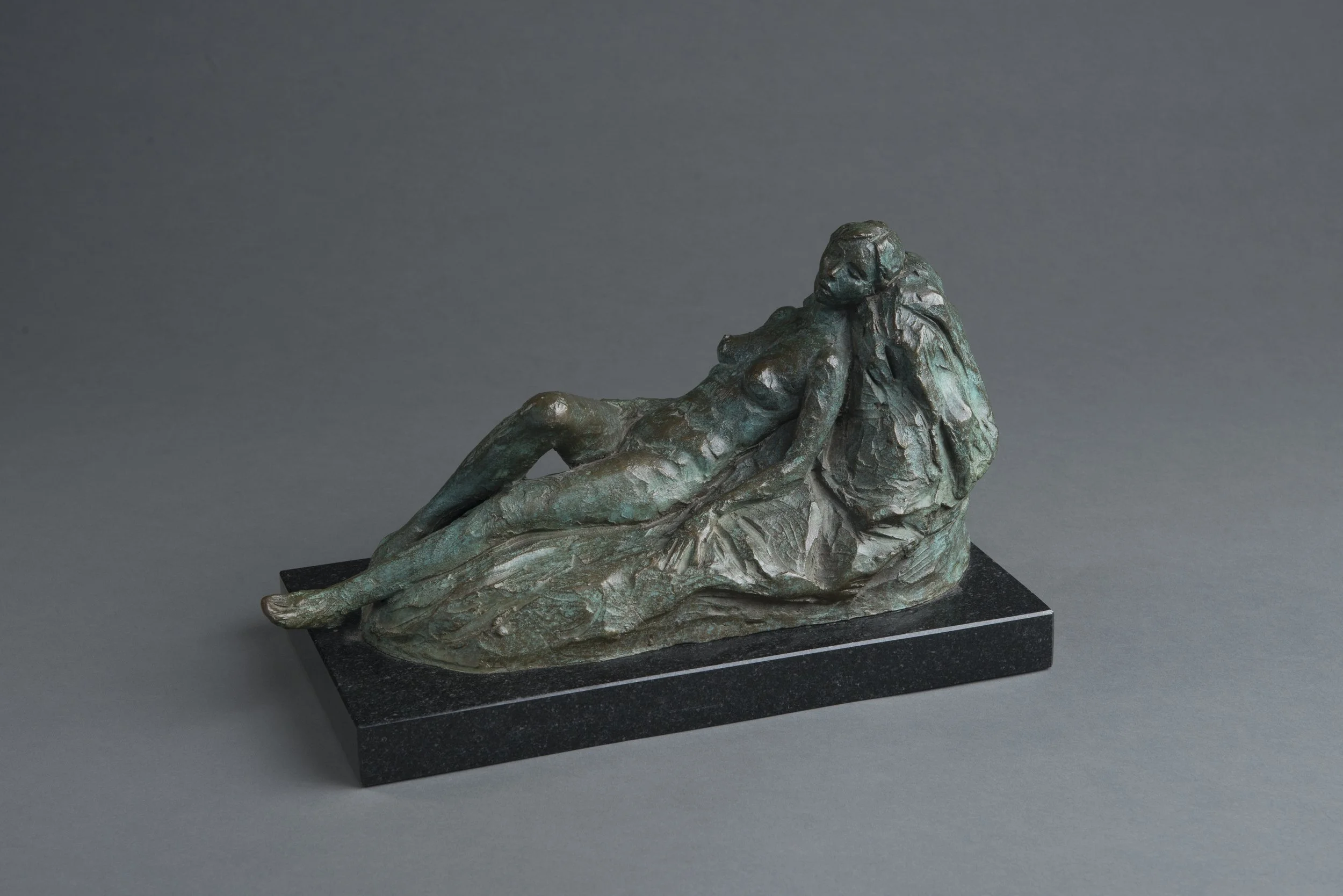 Bronze sculpture of a reclining woman resting her head on her arm, mounted on a black base.