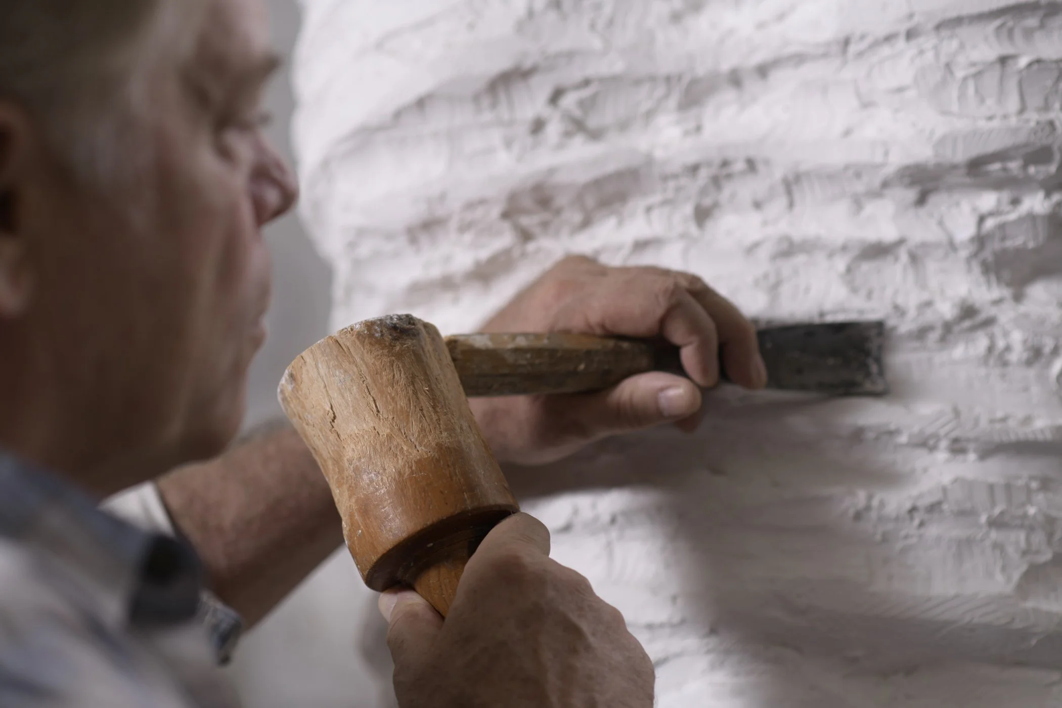 A person using a hammer to chisel white bricks on a wall.