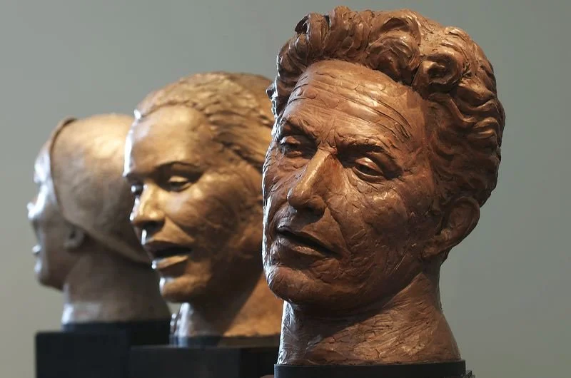 Three bronze busts of people exhibit front views, with the foremost bust having curly hair and detailed facial features.  Cultural Heroes