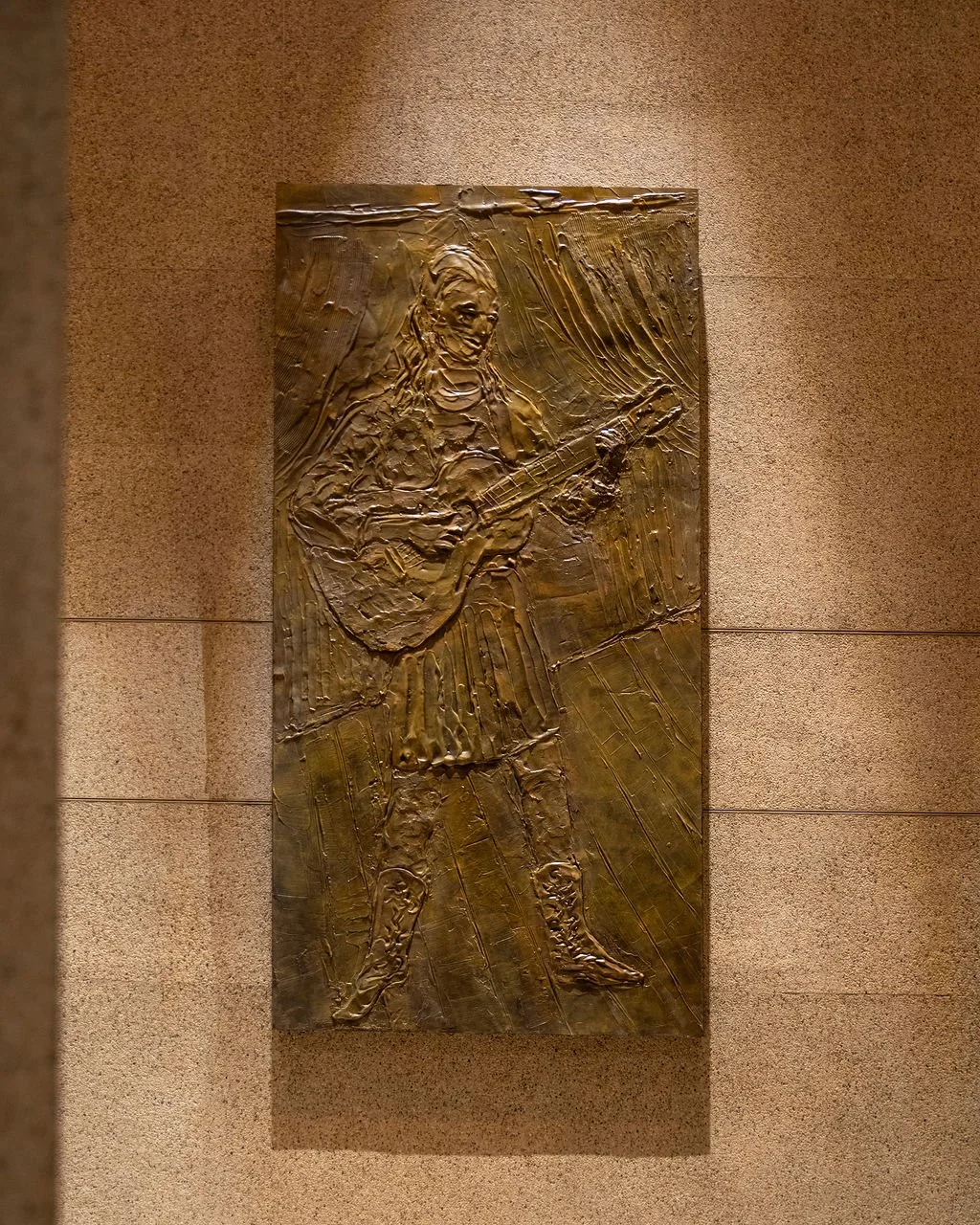 A bronze relief sculpture of a woman person playing a guitar, mounted on a wall.