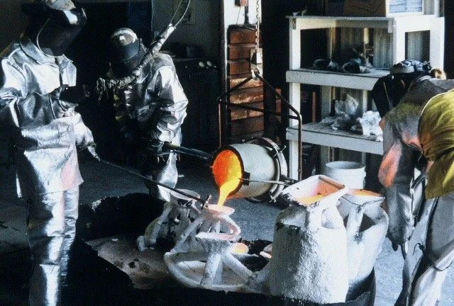 Glassblowers using a furnace to shape molten glass into a vessel in an industrial studio.
