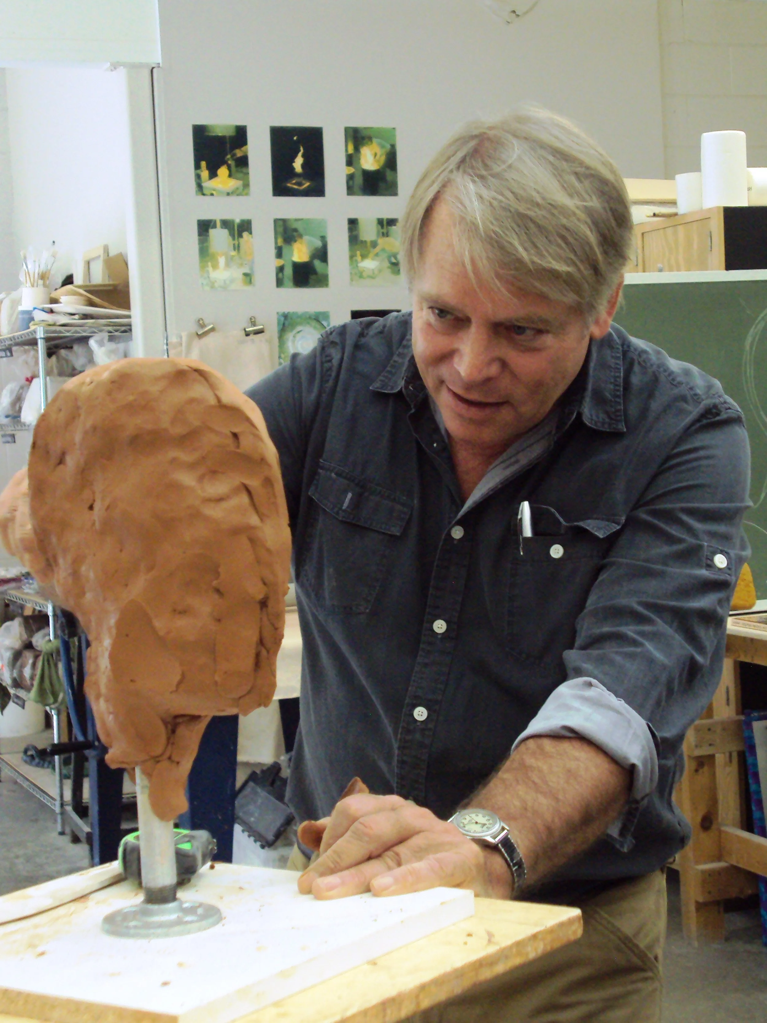 A man with gray hair and a watch is working on a sculpture in an art studio.