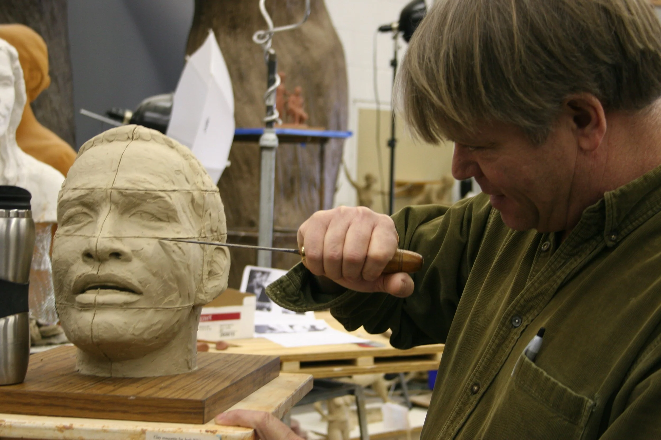A person carving a sculpture of a human face out of clay in a studio.