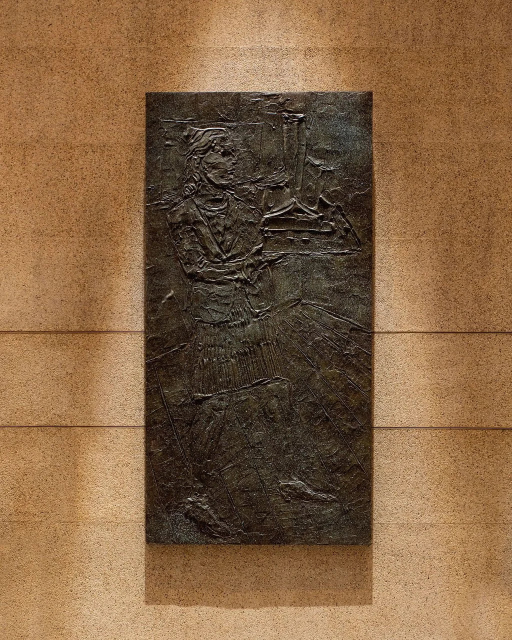 Raised relief artwork of a historical figure in armor, holding a sword, on a dark bronze plaque mounted on a wall.