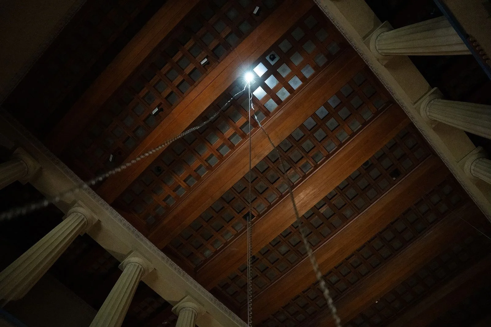 Looking up at a wooden ceiling with a bright light fixture in the center, surrounded by large columns.
