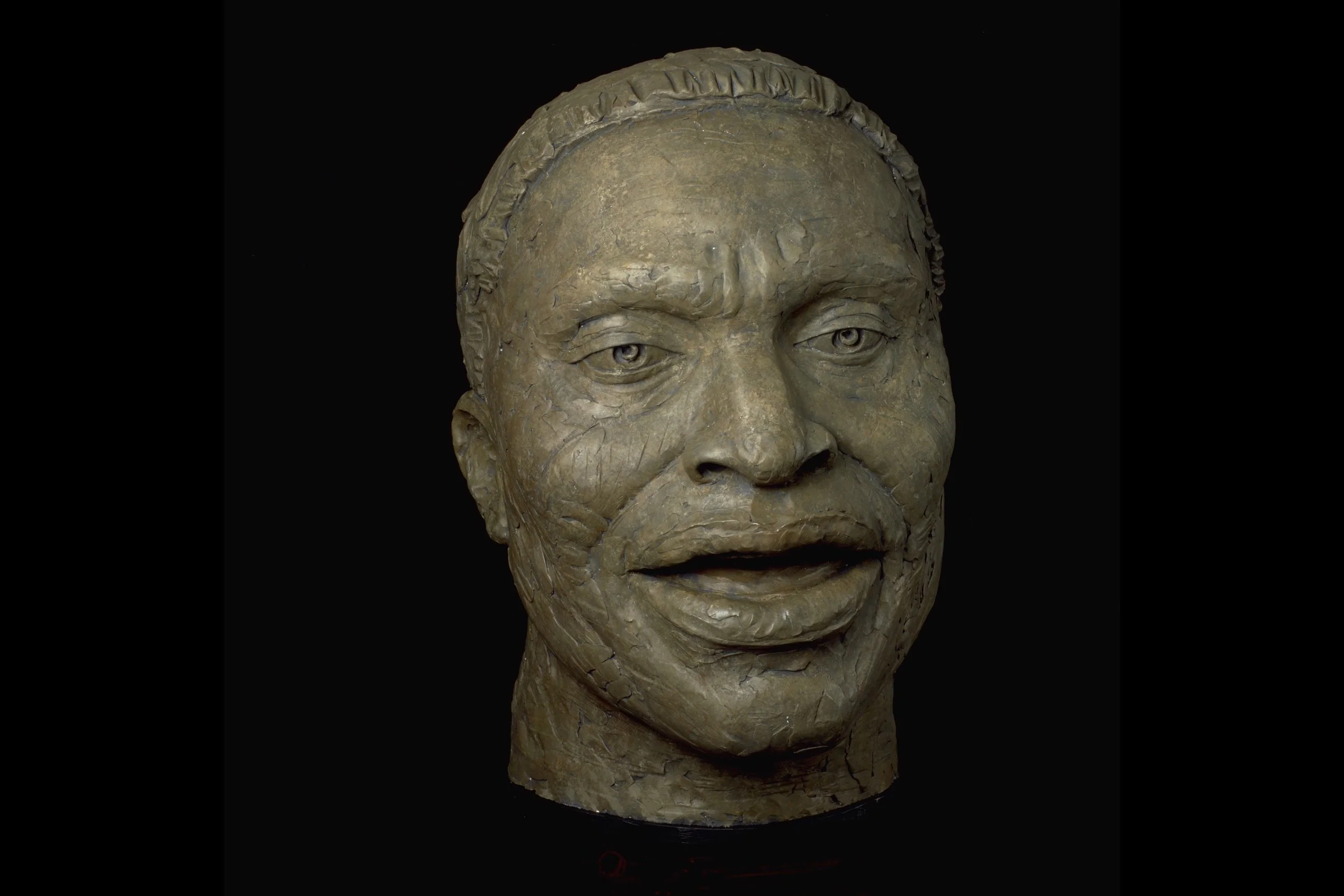Bronze bust sculpture of a man with detailed facial features and textured hair against a black background.